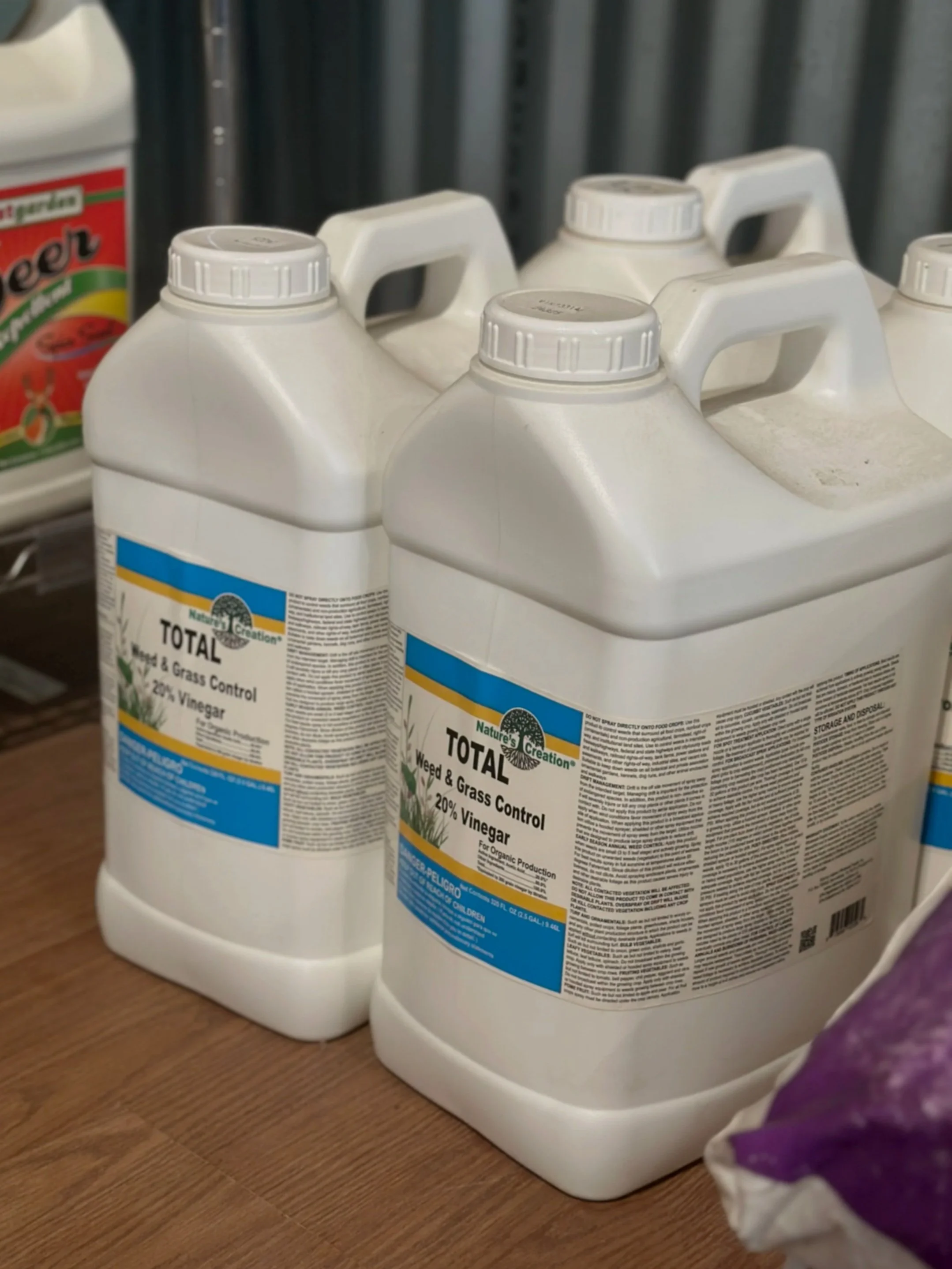 Two large white bottles of Nature's Creation Total Weed & Grass Control with 20% Vinegar on a wooden surface.