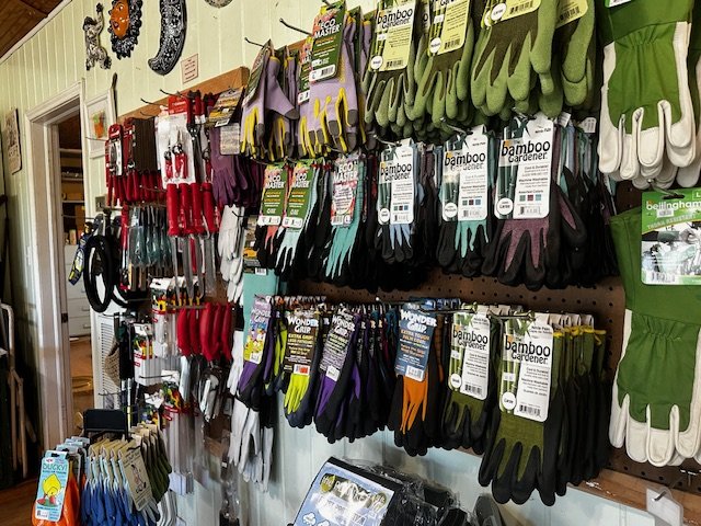 Display of gardening gloves hanging on a wall at a store, with different colors and styles, including bamboo and rubber gloves.