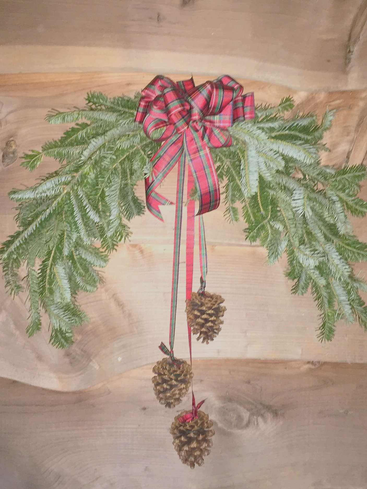 Decorative pine branch with a red plaid ribbon and three hanging pinecones.