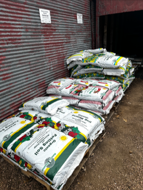 Stacked bags of garden soil or mulch outside a building with a metal shutter.
