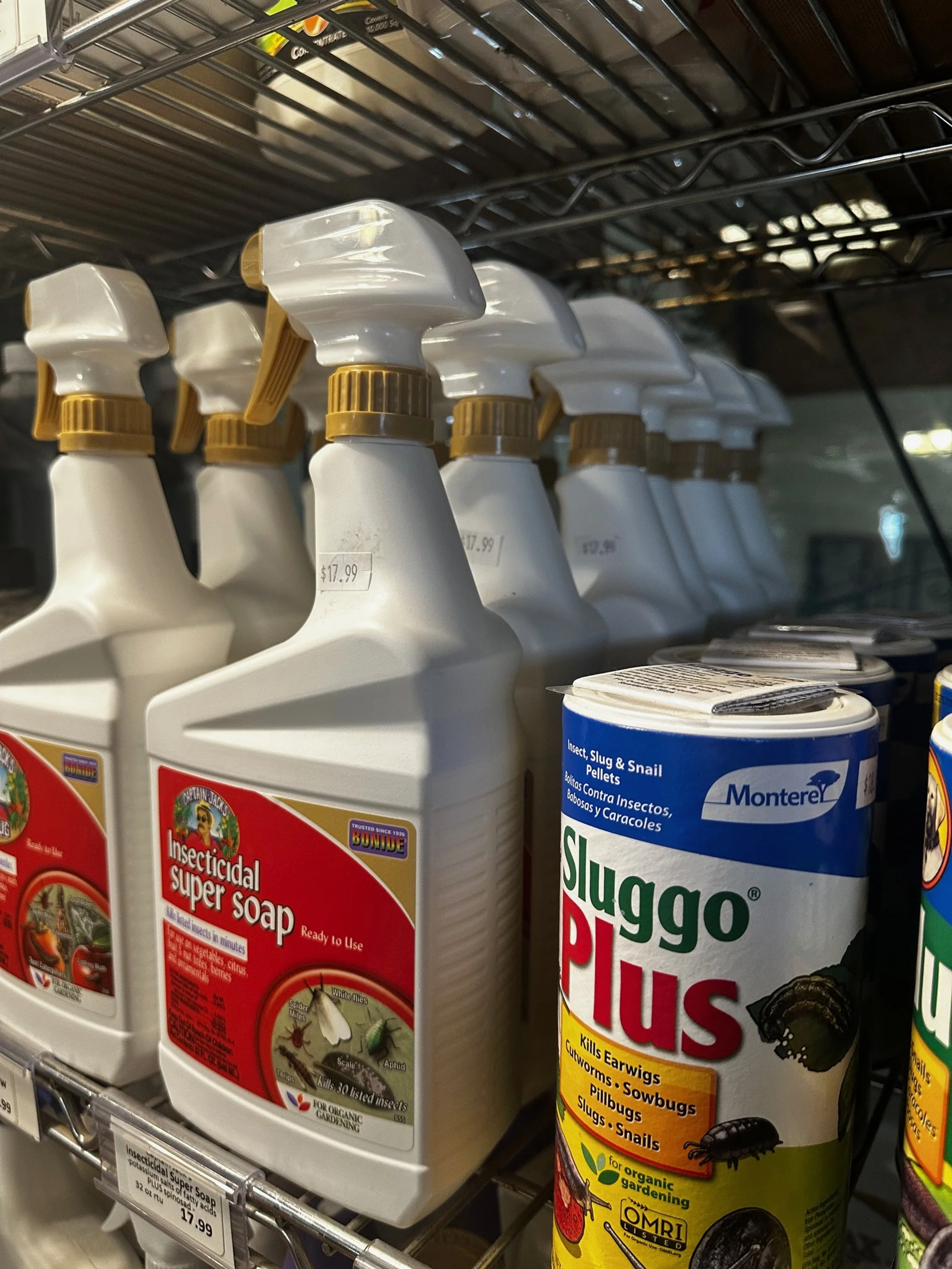 A store shelf with bottles of insecticide super soap and mice bait called Slugo Plus. The bottles are white with spray nozzles, and the Slugo Plus container is cylindrical with a label showing insects and pest control information.