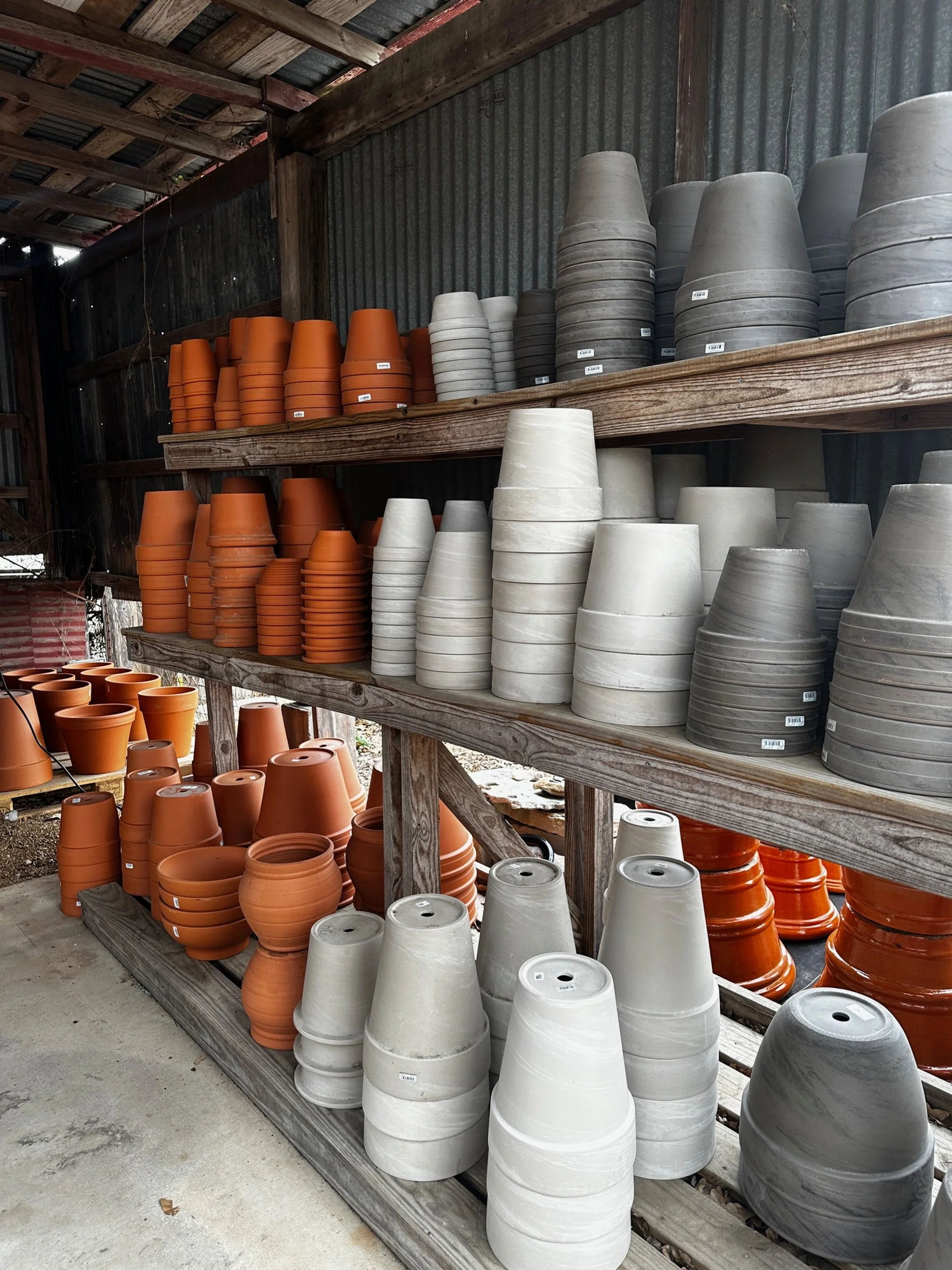 Shelves filled with stacked terracotta, white, and gray flower pots in a garden center or nursery.