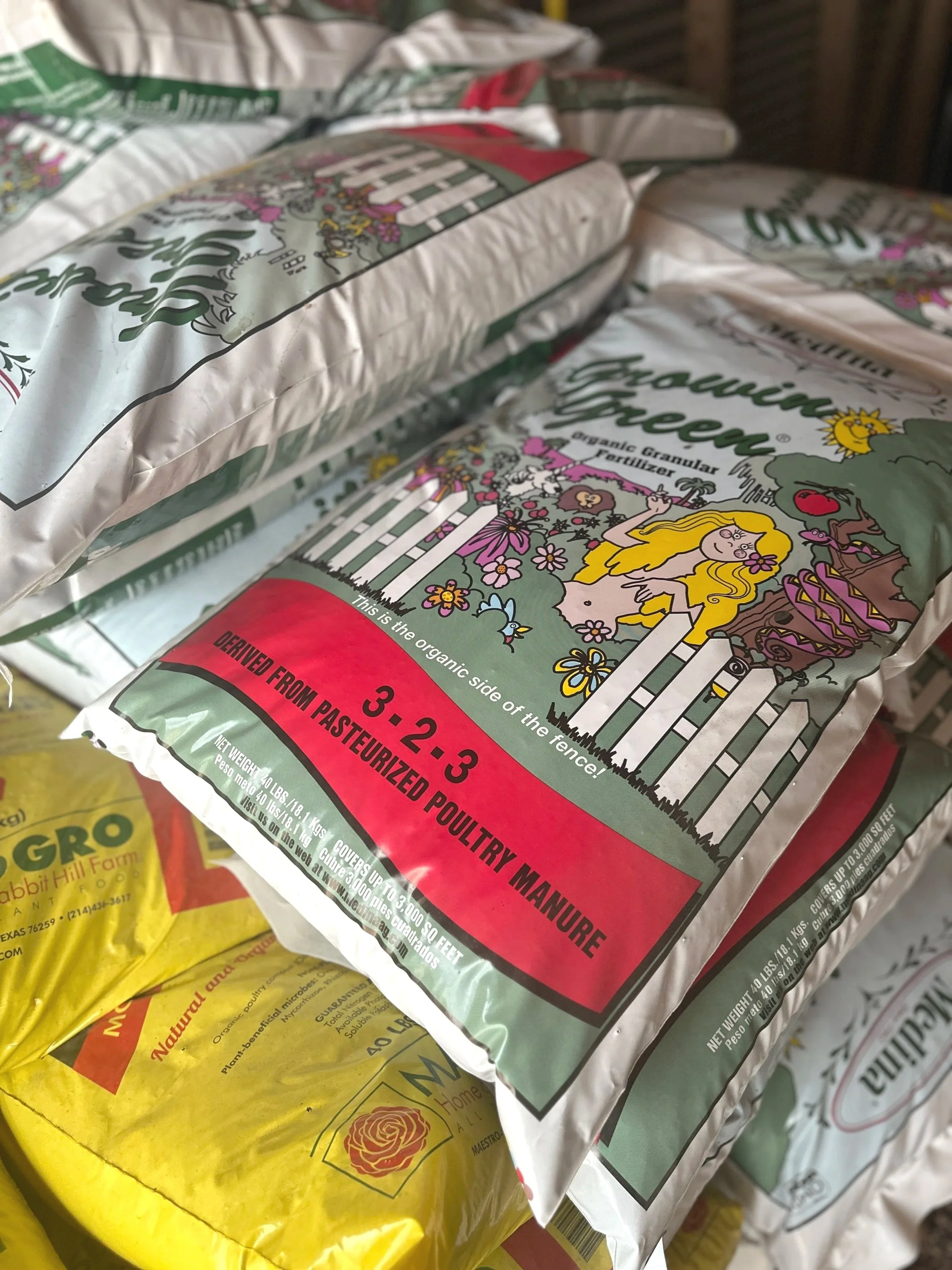 Bag of organic granular fertilizer with illustrated garden scene and a white picket fence, labeled as derived from pasteurized poultry manure.