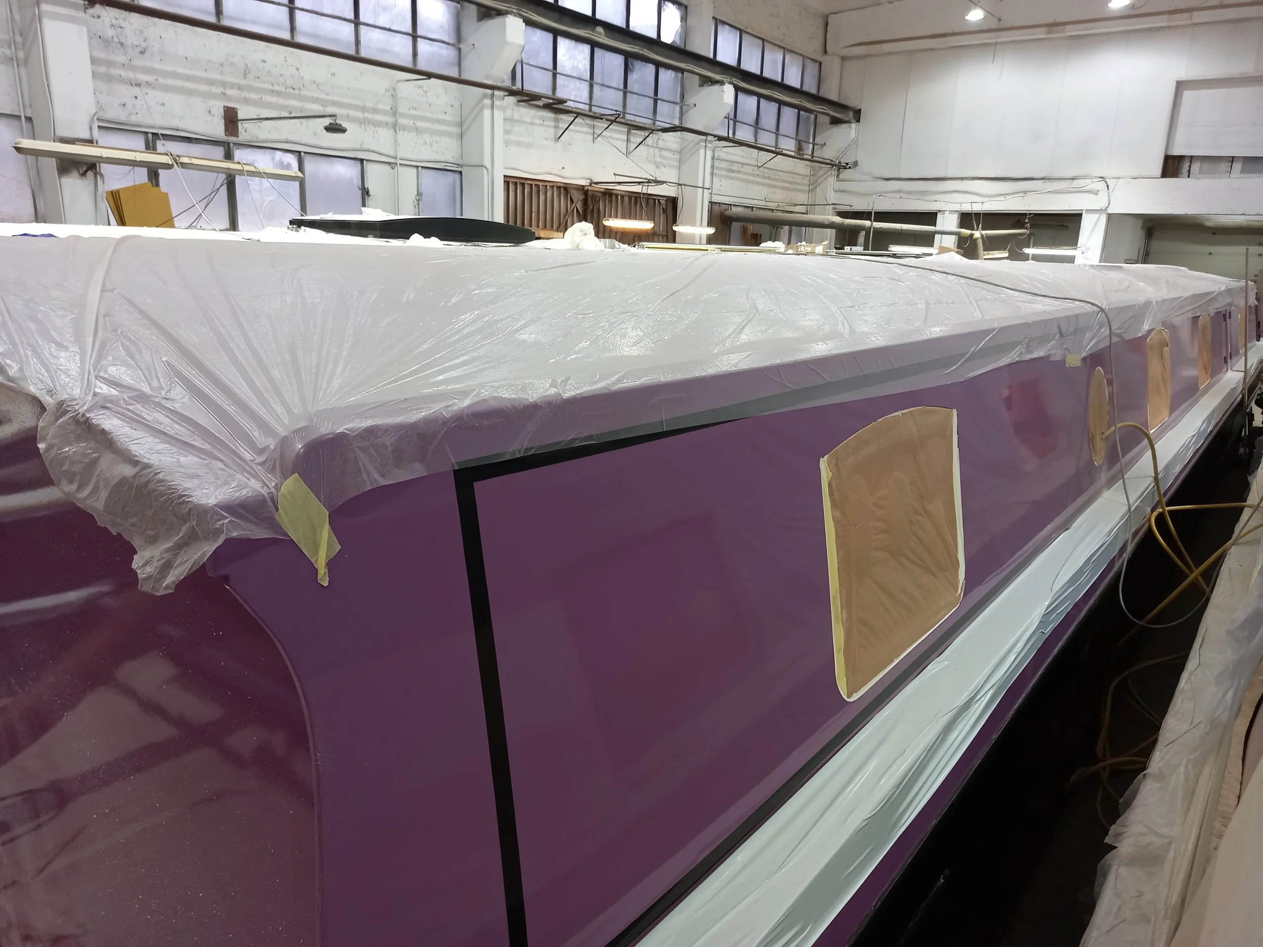 A boat inside a workshop, covered with plastic protective sheets and taped windows, in the process of being painted or repaired.