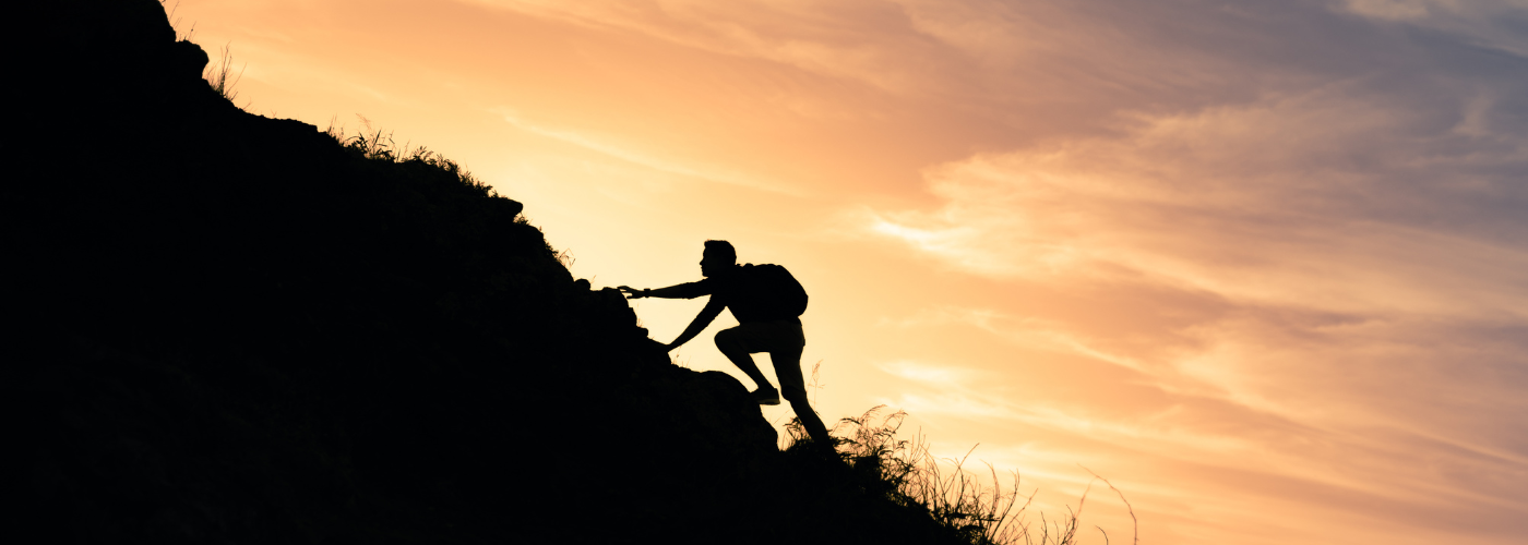 Silhouette of a person rock climbing during sunset with a backpack.