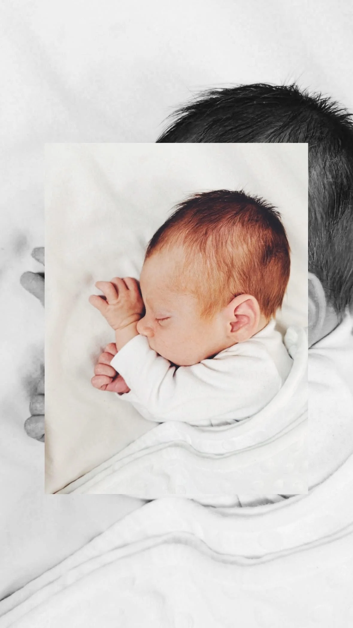 A sleeping infant with red hair, curled up on a white blanket, with eyes closed and hands near the face.