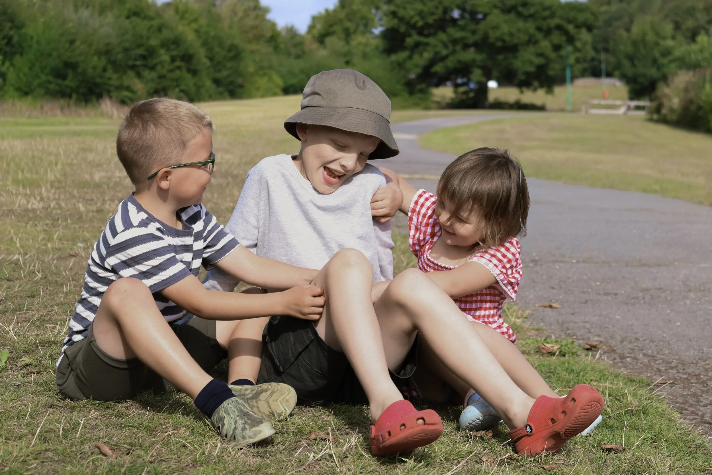 Three children sitting on the grass outdoors, playing and laughing with each other.