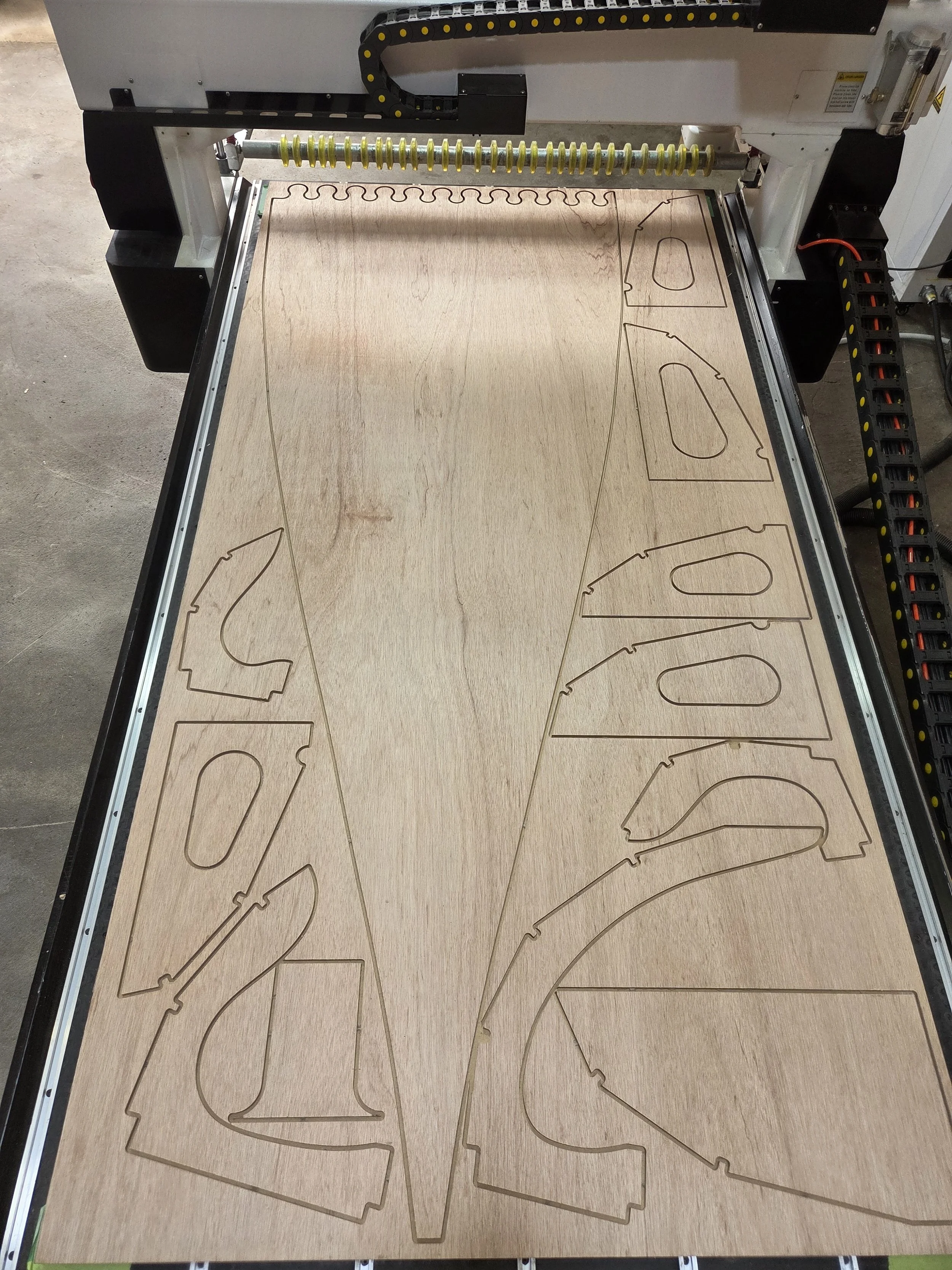 Laser cutout pieces of wood in the shape of guitar bodies on a wooden surface.