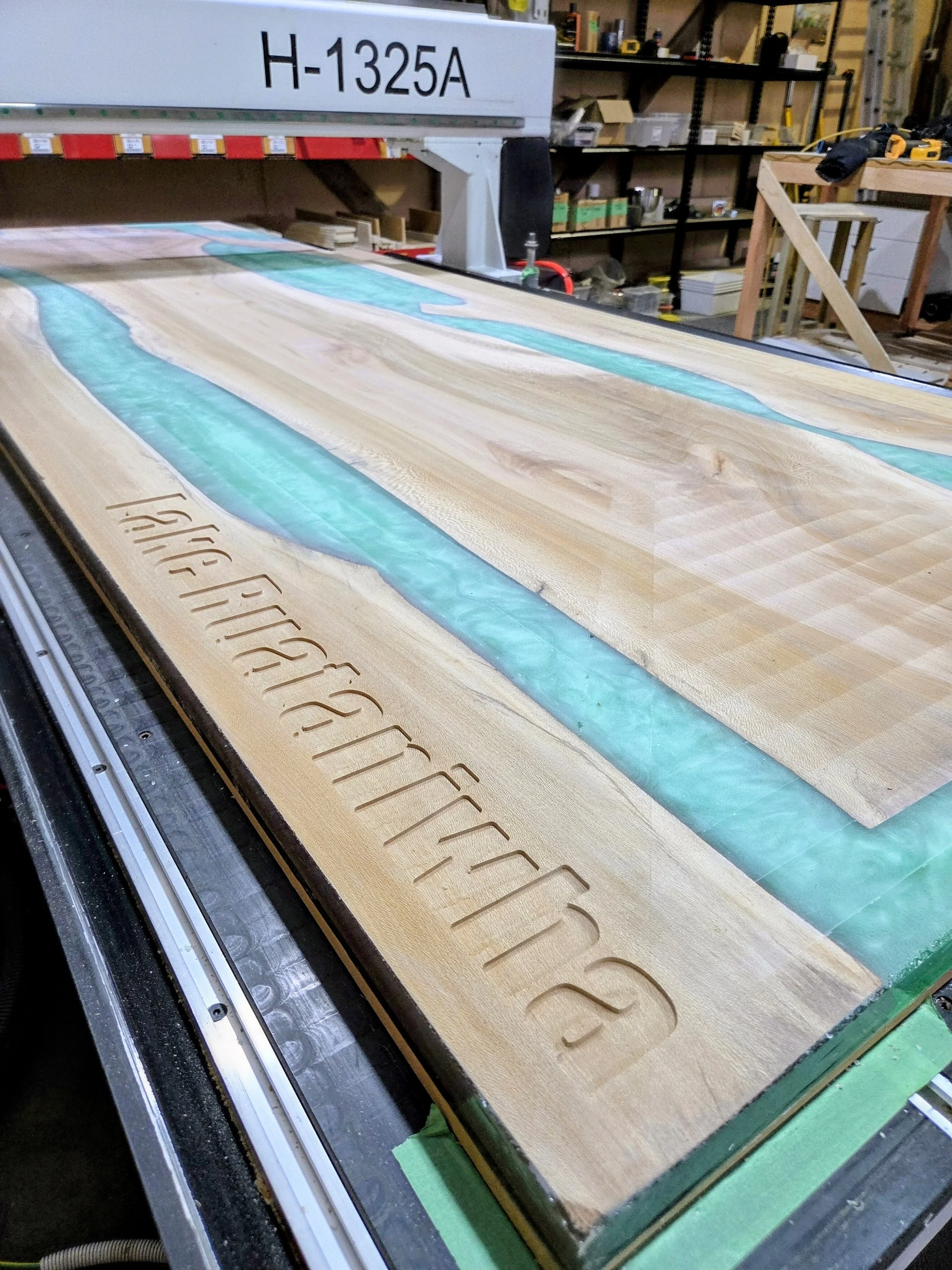 Close-up of a woodworking CNC router machine cutting the word 'SPECHT' into a piece of wood with flowing water and a workshop background.