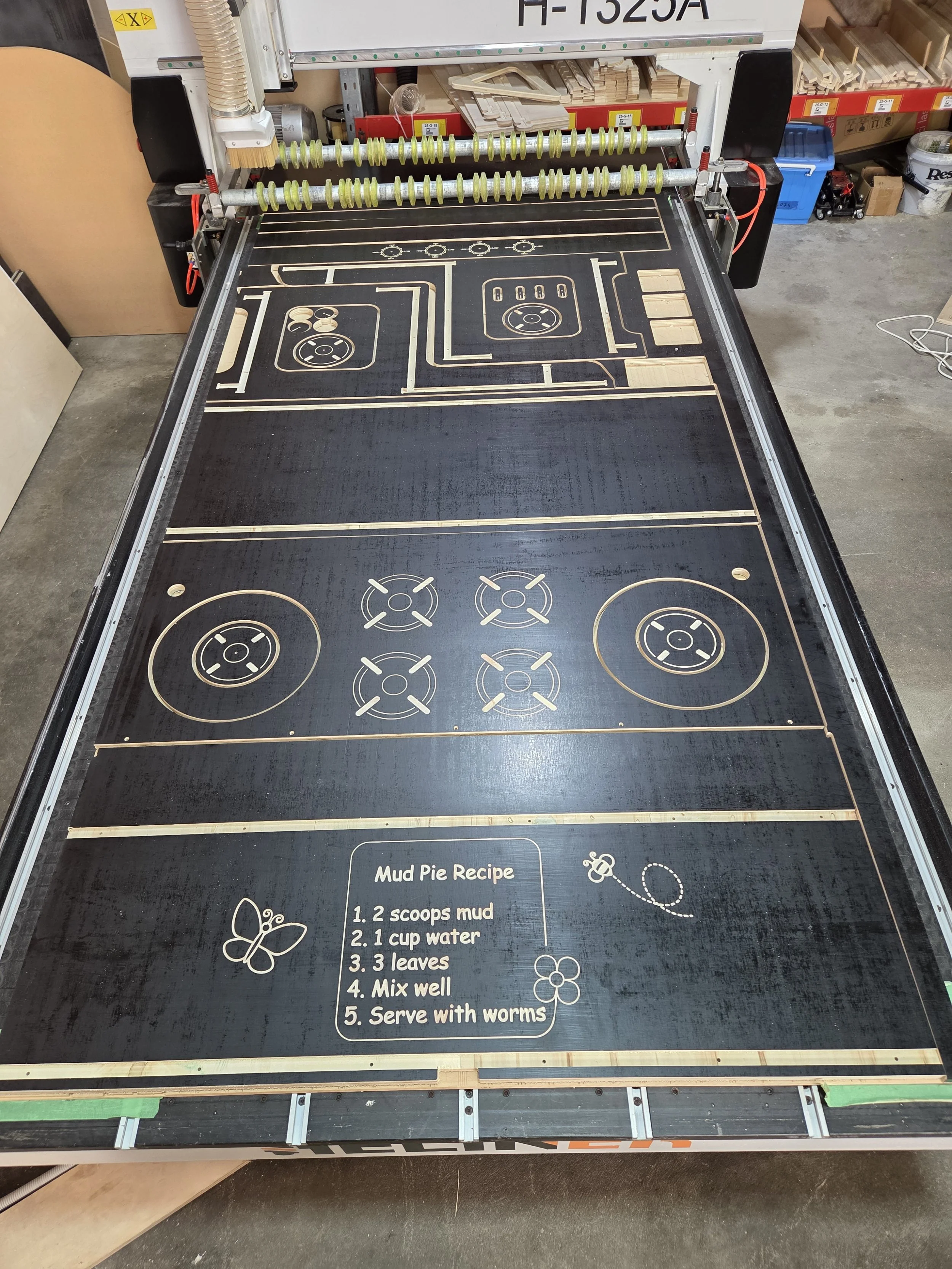 A woodworking CNC machine with a black work surface and a visual recipe for making mud pie, including ingredients and instructions.