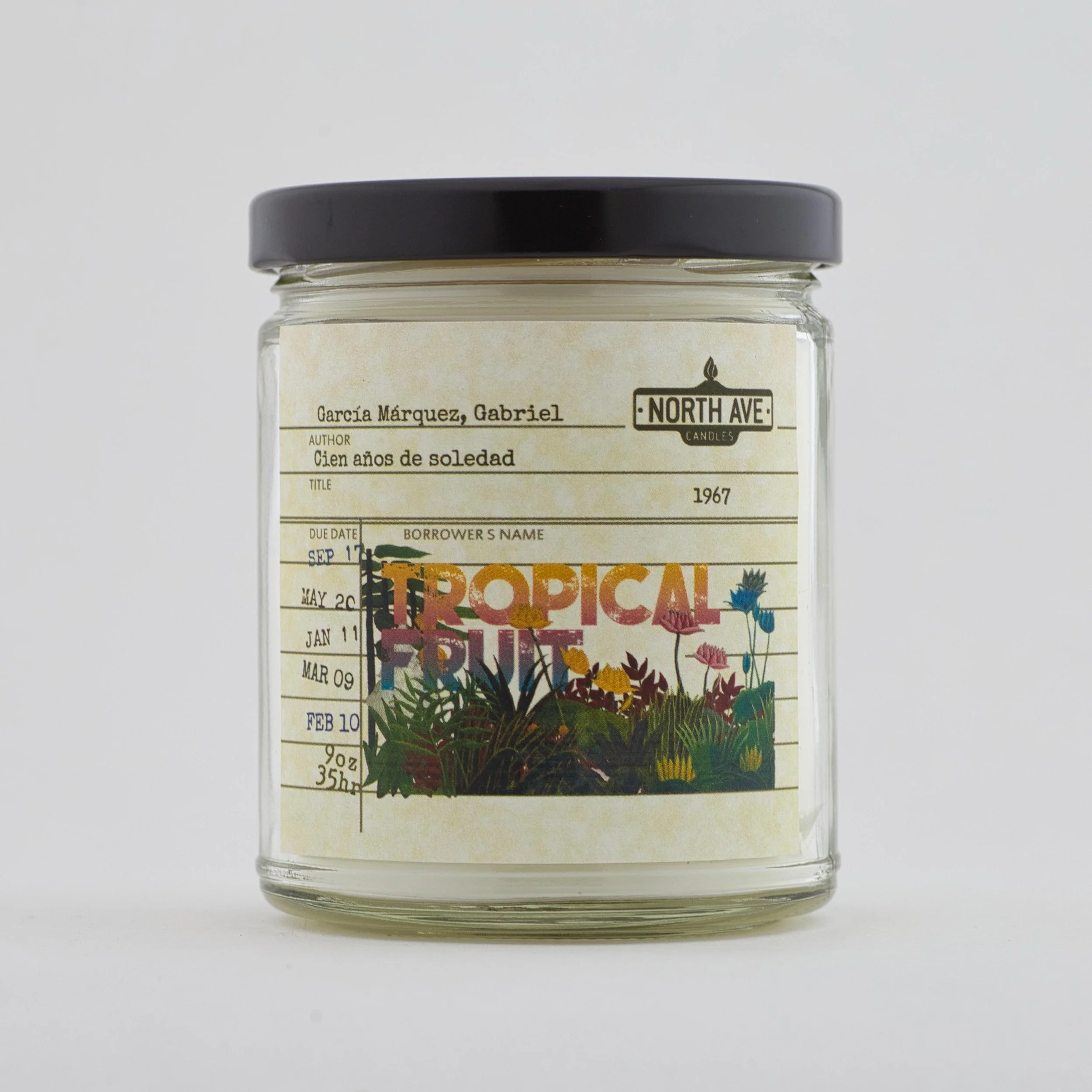 A glass jar with a black lid containing a candle with a label that reads 'Tropical Fruit' and features colorful illustrations of tropical plants and flowers. The jar also has a vintage-style label with handwritten details including the author, title,