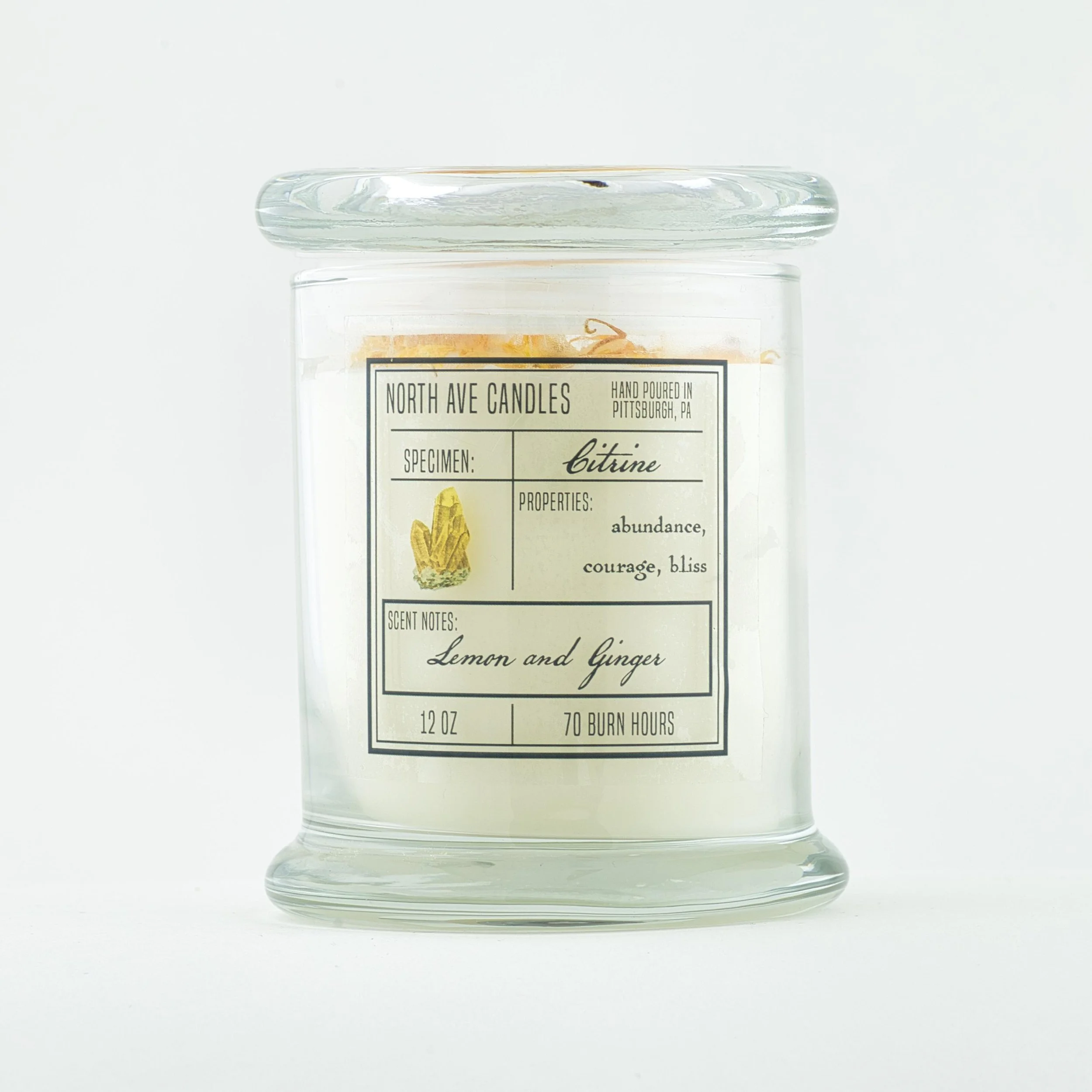 A white candle in a clear glass jar with a label indicating it is a Citrine scented candle by North Ave Candles, with scent notes of lemon and ginger, and a burn time of 70 hours.