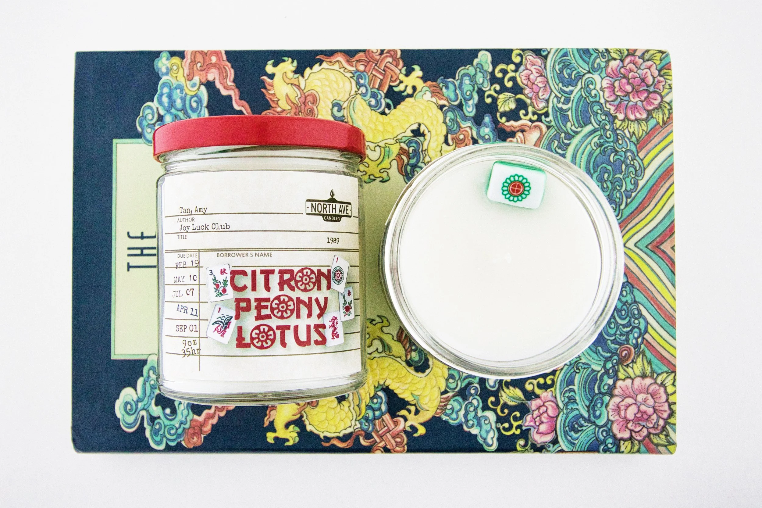 Decorative book cover with a yellow dragon, flowers, and clouds. Two glass jars with pink and green lids—one has a label with handwritten notes and a sticker reading "Citron Peony Lotus".