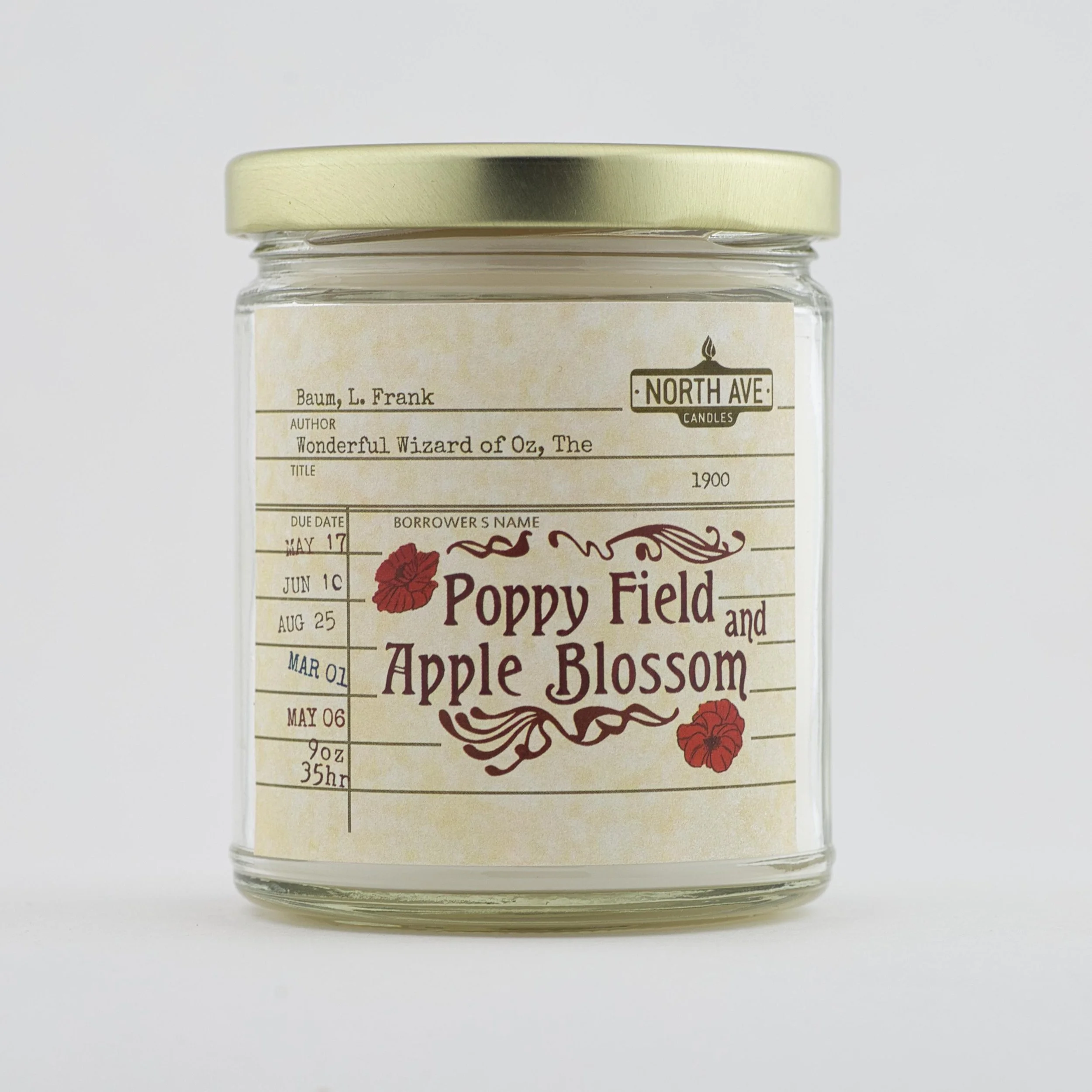 A glass jar candle with a beige label featuring red flowers and black text, including a book and author pattern, and titled "Poppy Field and Apple Blossom."