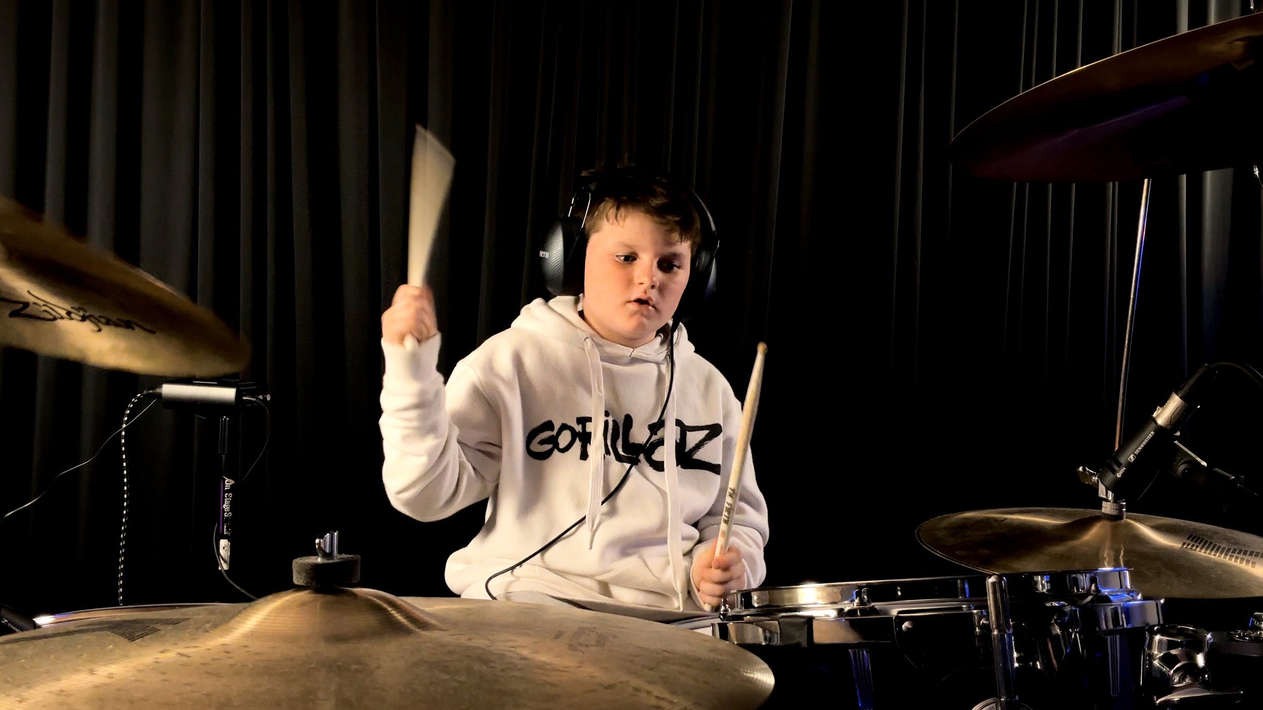 Young boy with headphones playing drums in a soundproof music studio.