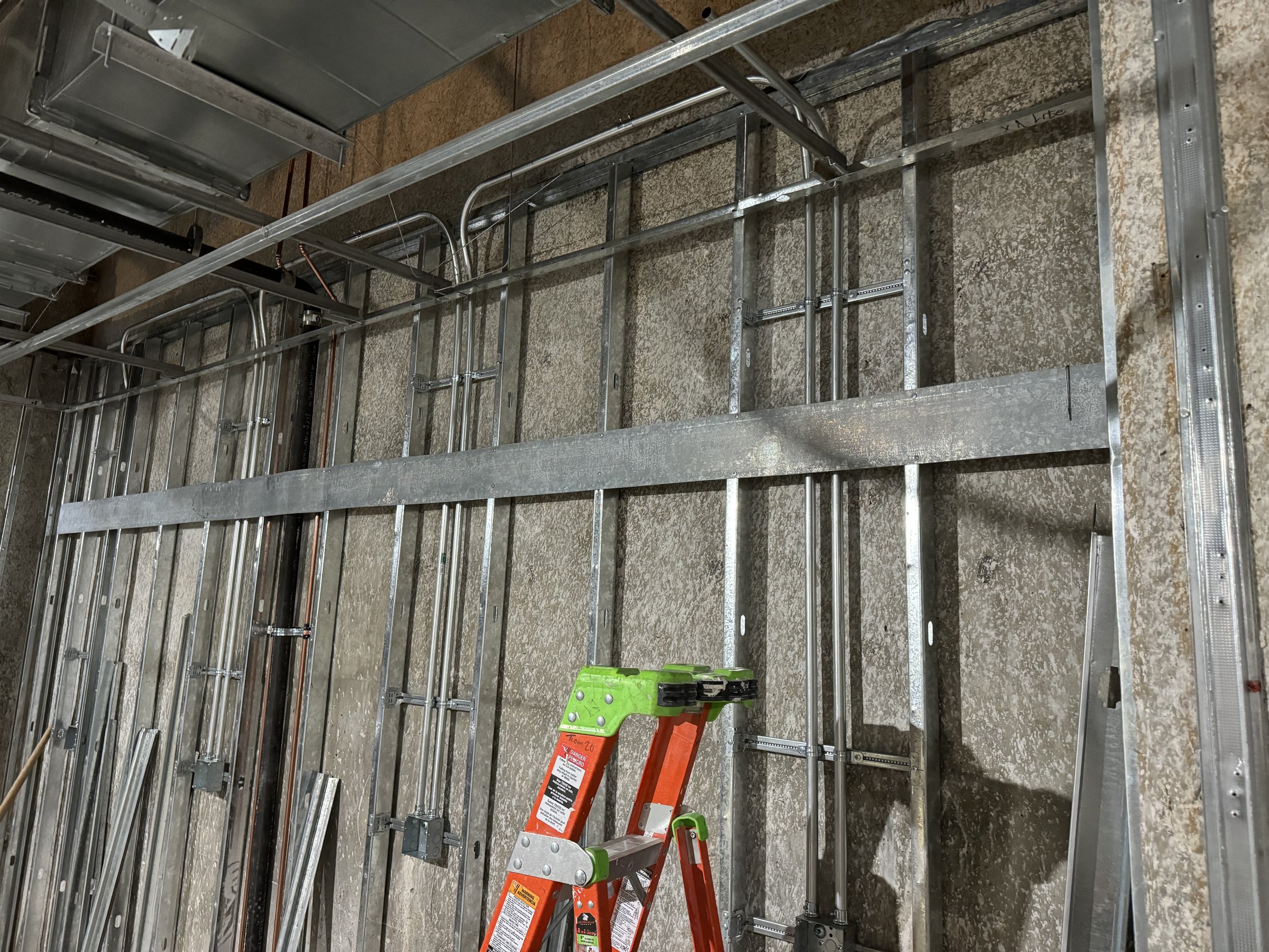 Steel framing structure on a construction site with a green and orange step ladder in the foreground.