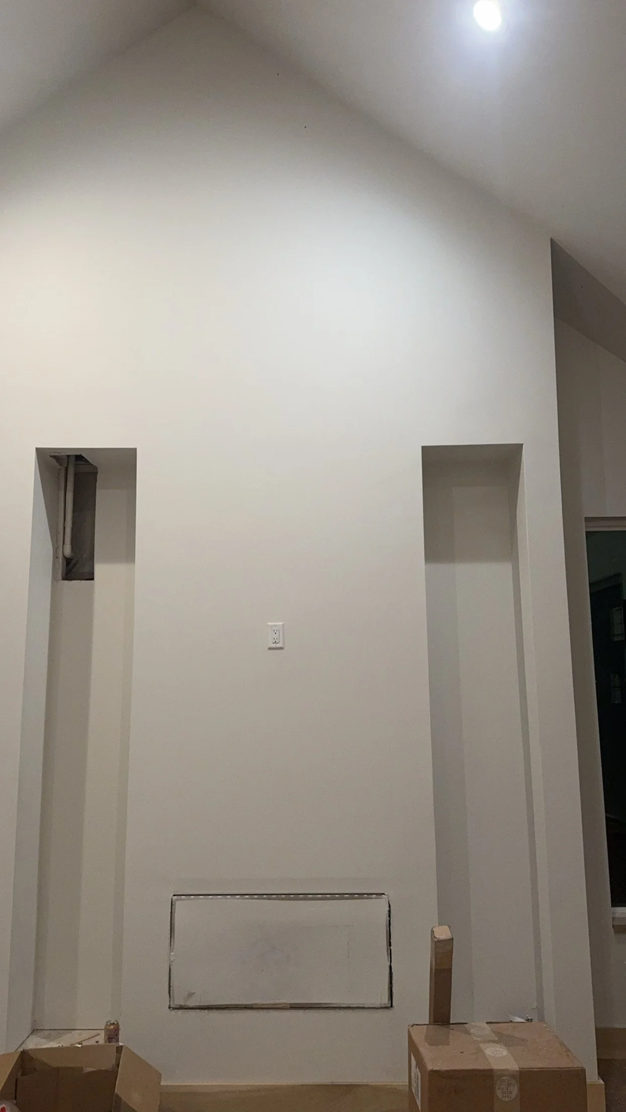 Interior wall with two narrow vertical wall cutouts and a partially covered vent or access panel at the bottom, with construction boxes on the floor.