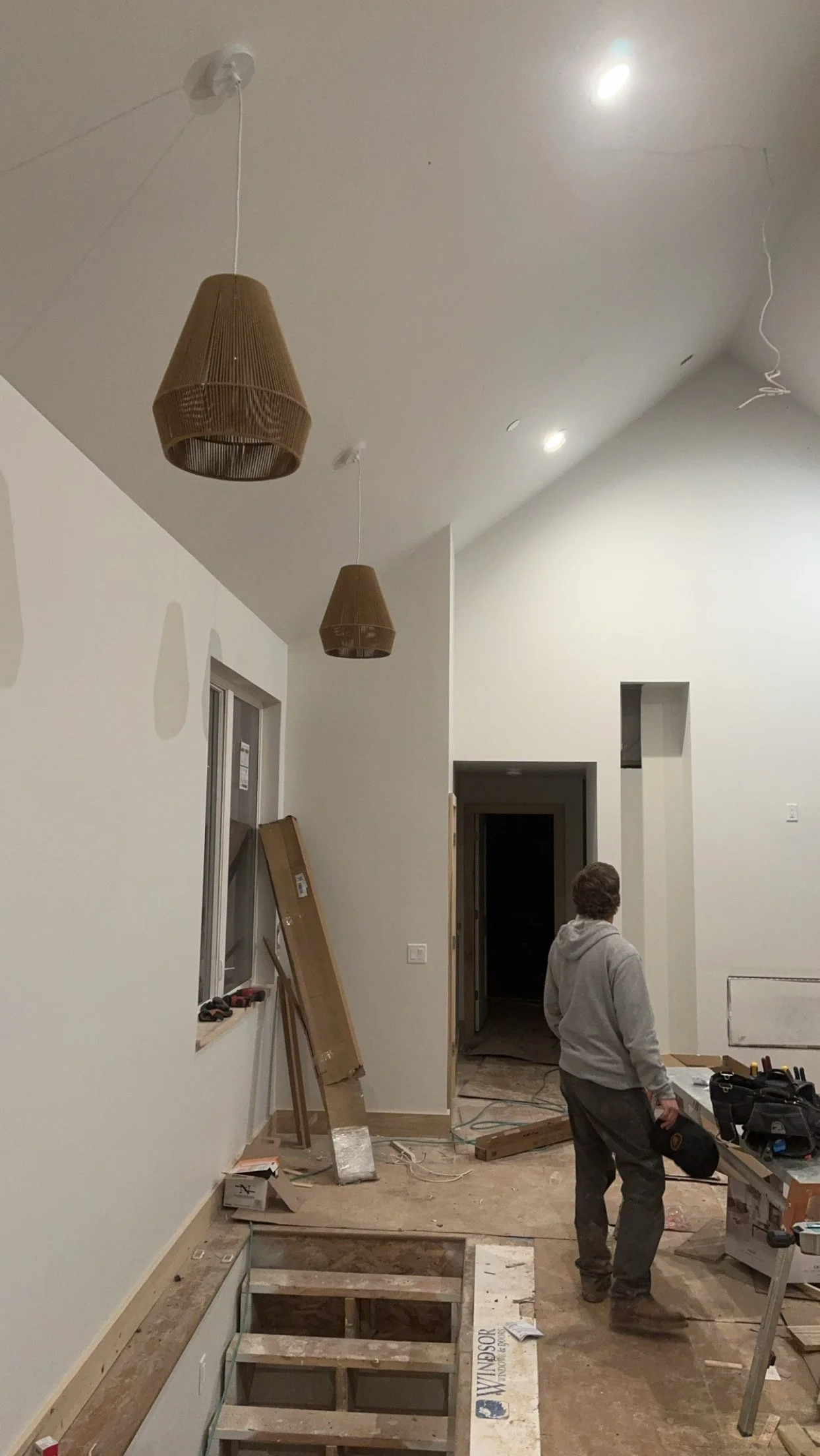 Interior of a house under construction with unfinished flooring, hanging pendant lights and construction tools.
