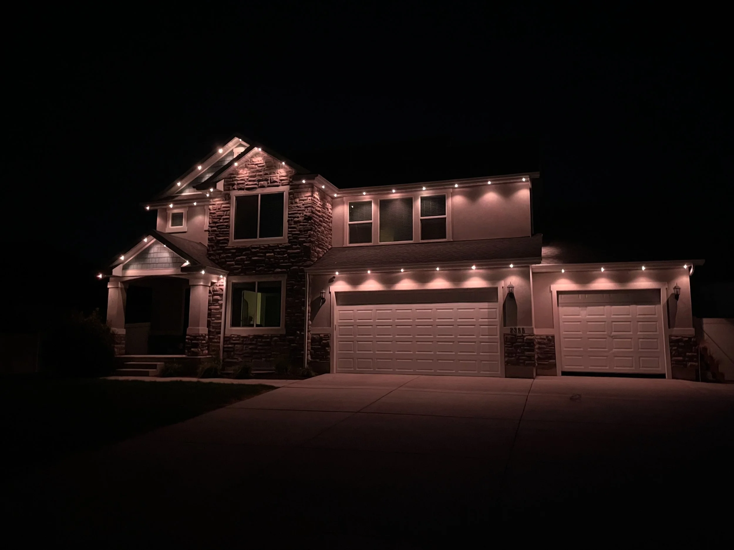 A two-story house illuminated with string permanent lighting, visit for all of your lighting needs!