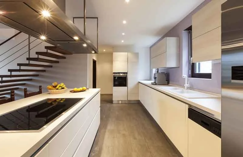 Modern kitchen with white cabinets, black stovetop on island, stainless steel refrigerator, wall oven, microwave, and double sink near window.