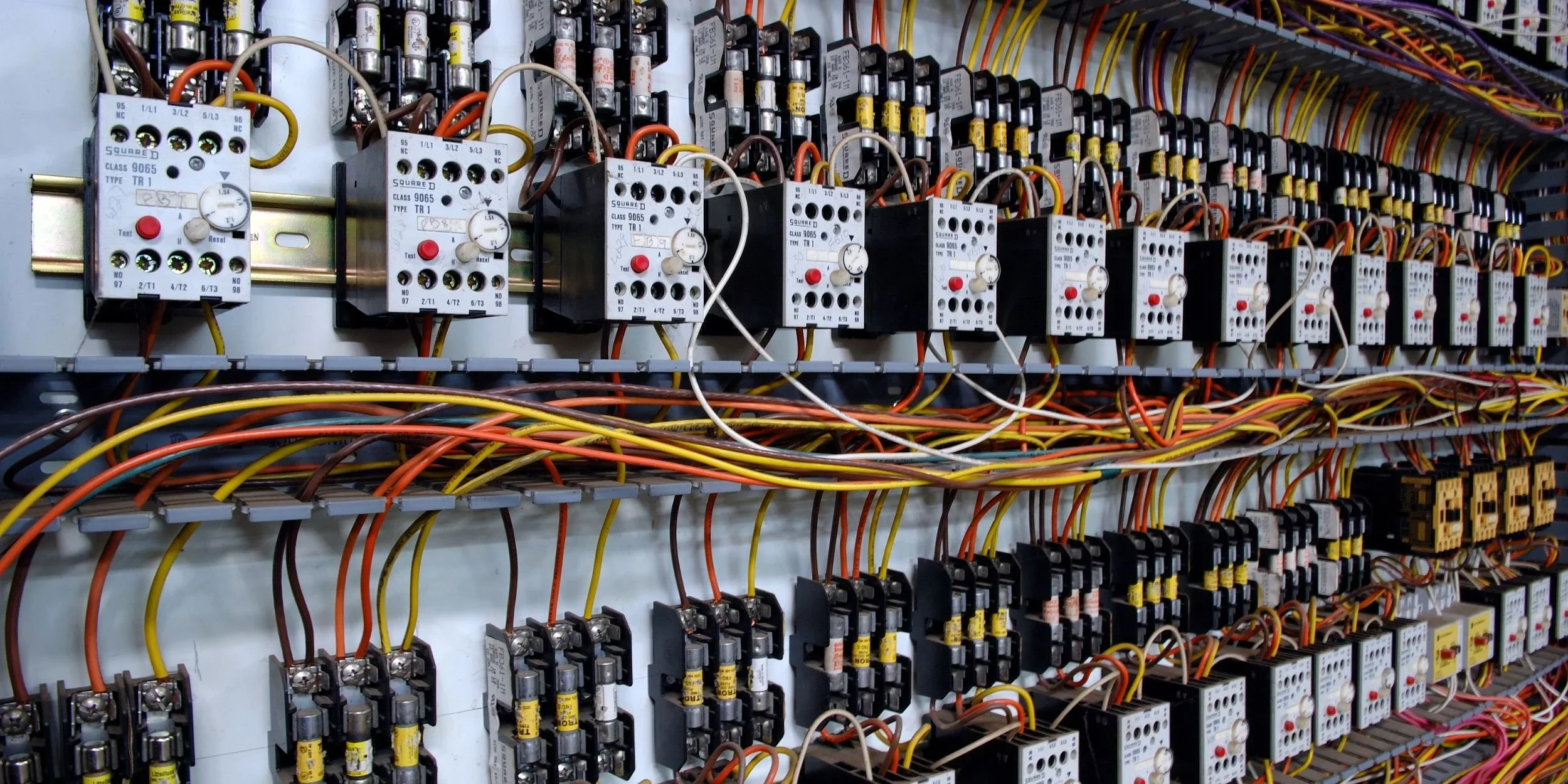 Electrical control panel with numerous relays, wires, and components arranged in rows.