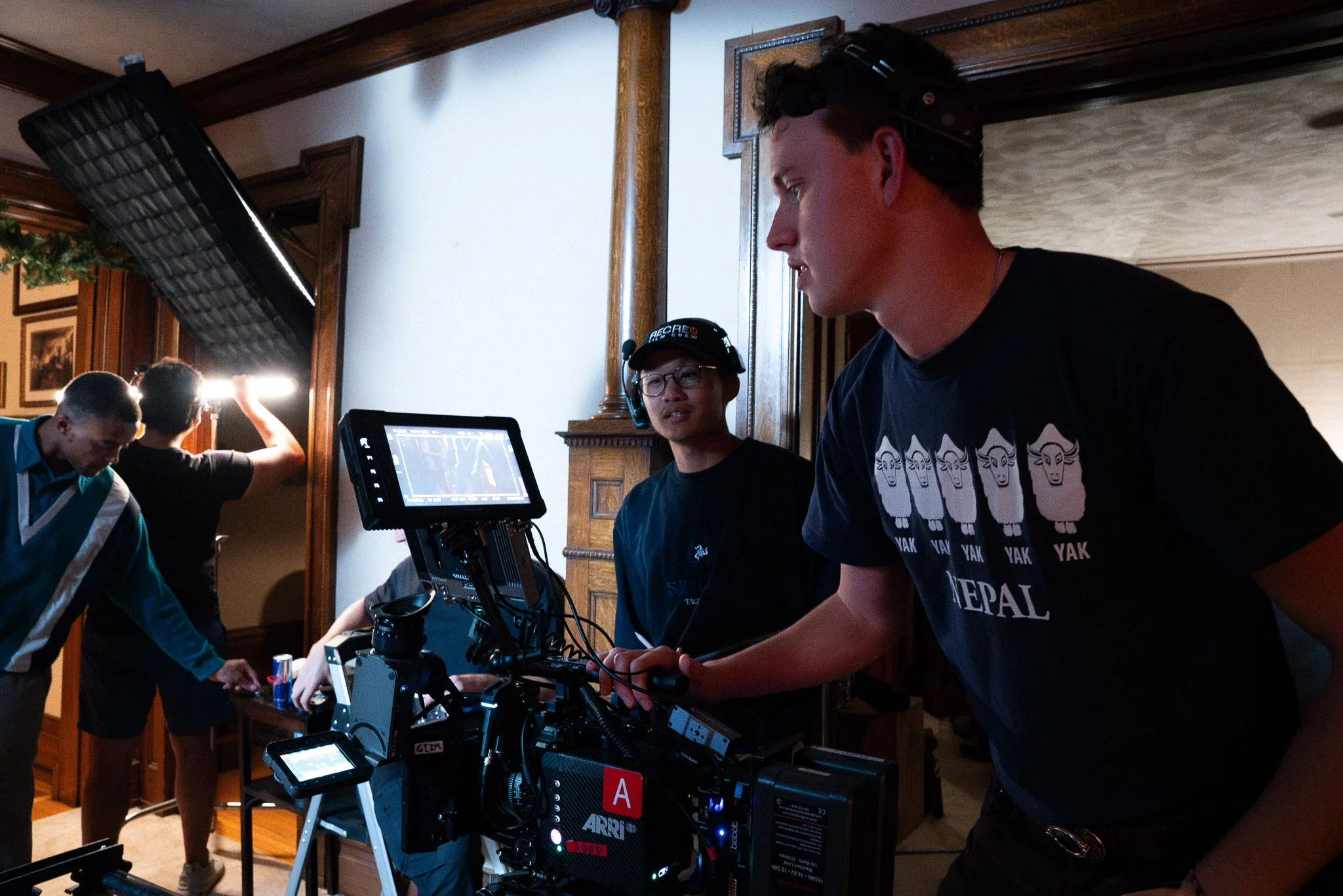 Film crew setting up camera on set, with crew members preparing equipment and lighting inside a room.