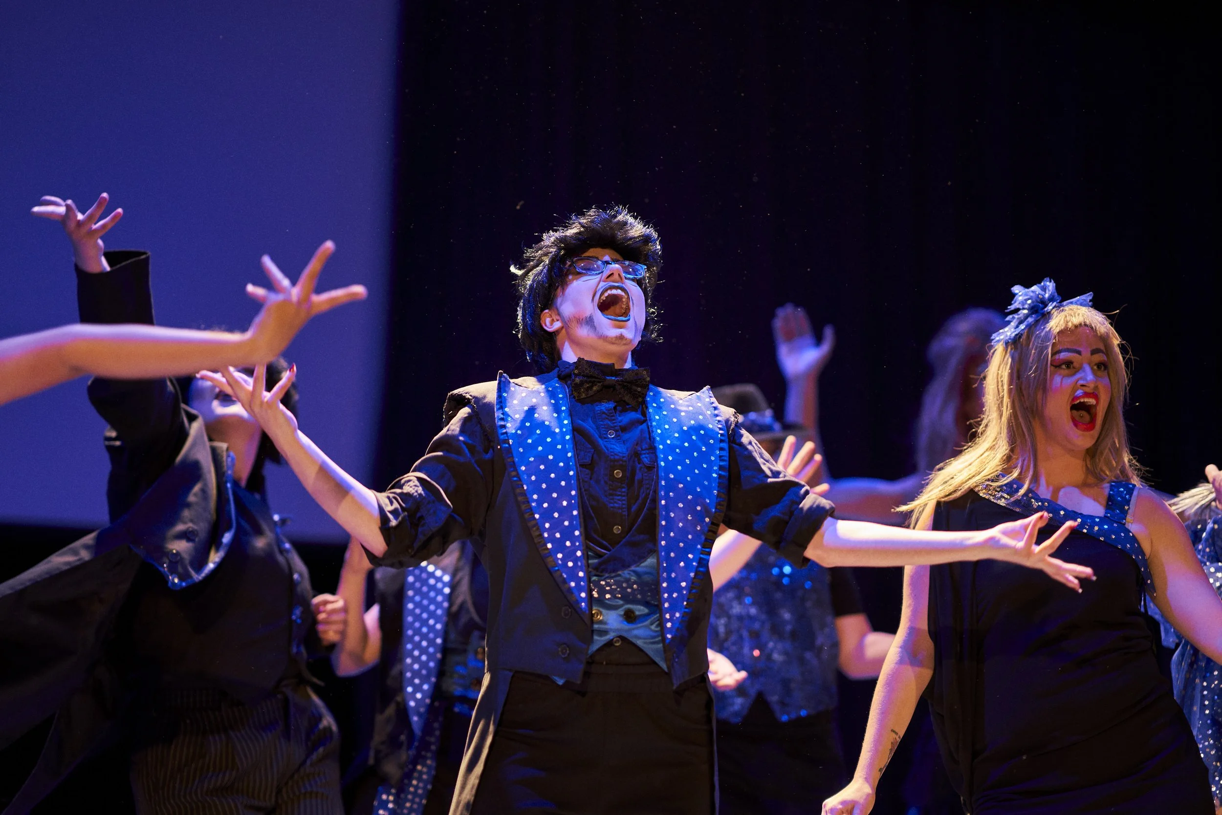 People performing on stage, singing passionately, with expressive gestures and colorful costumes under stage lighting.