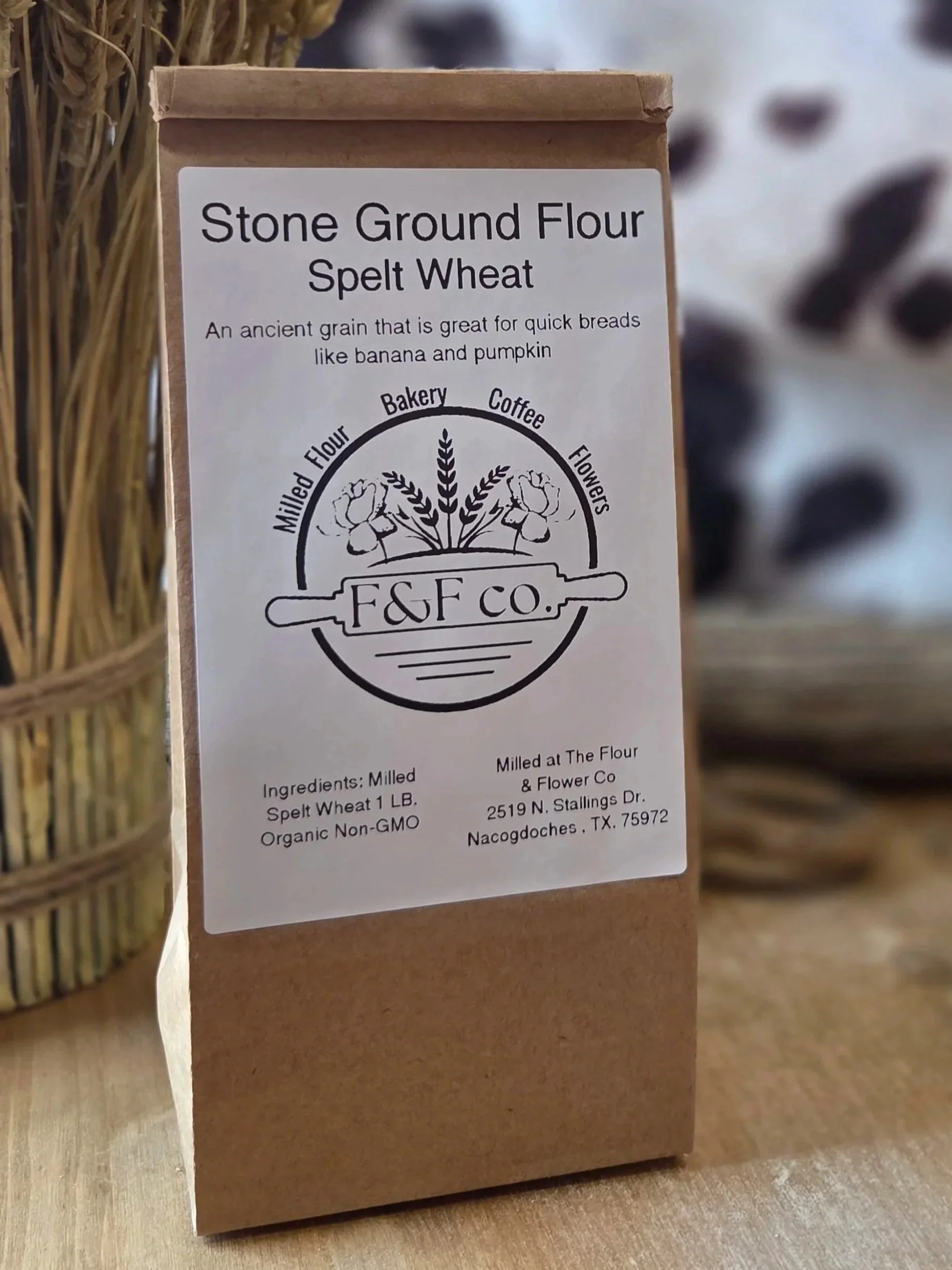 A brown paper bag of stone ground flour labeled 'F&F Co.' with a logo featuring wheat and flowers, stating 'Spelt Wheat' and that it is suitable for quick breads like banana and pumpkin. The label provides ingredients, weight, and company details.