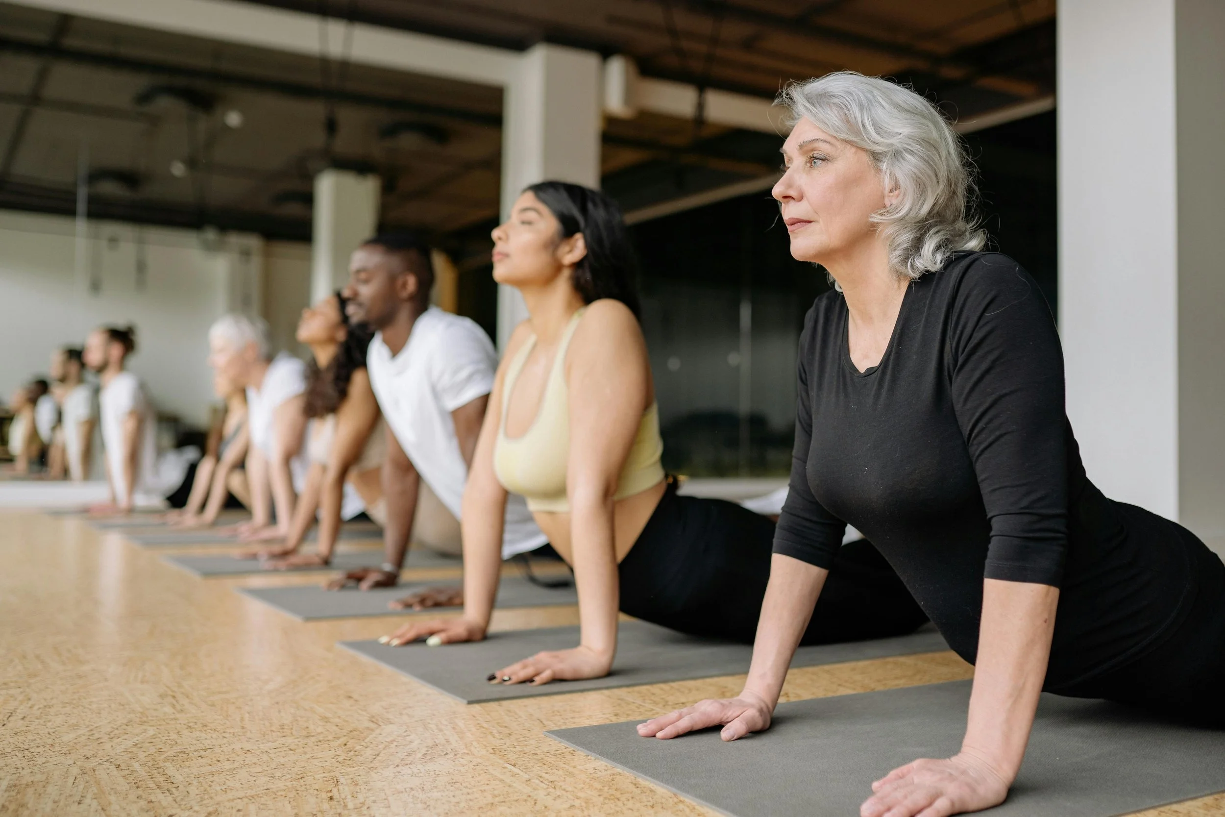 A diverse group of people in a yoga class, practicing pose on mats in a spacious studio.