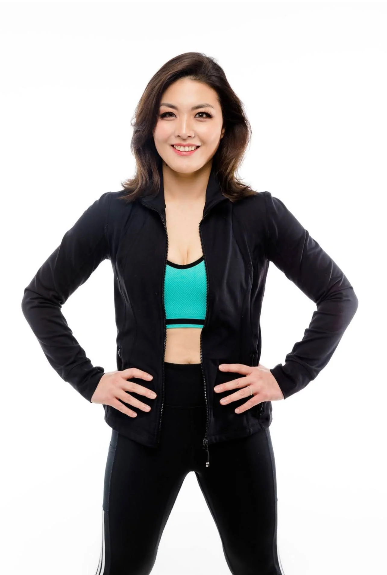 Linda Kim in athletic wear standing with hands on hips, smiling, against a plain white background.