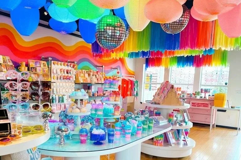 Colorful store display with rainbow decorations, paper lanterns, and disco balls, showcasing various party supplies and decorations.