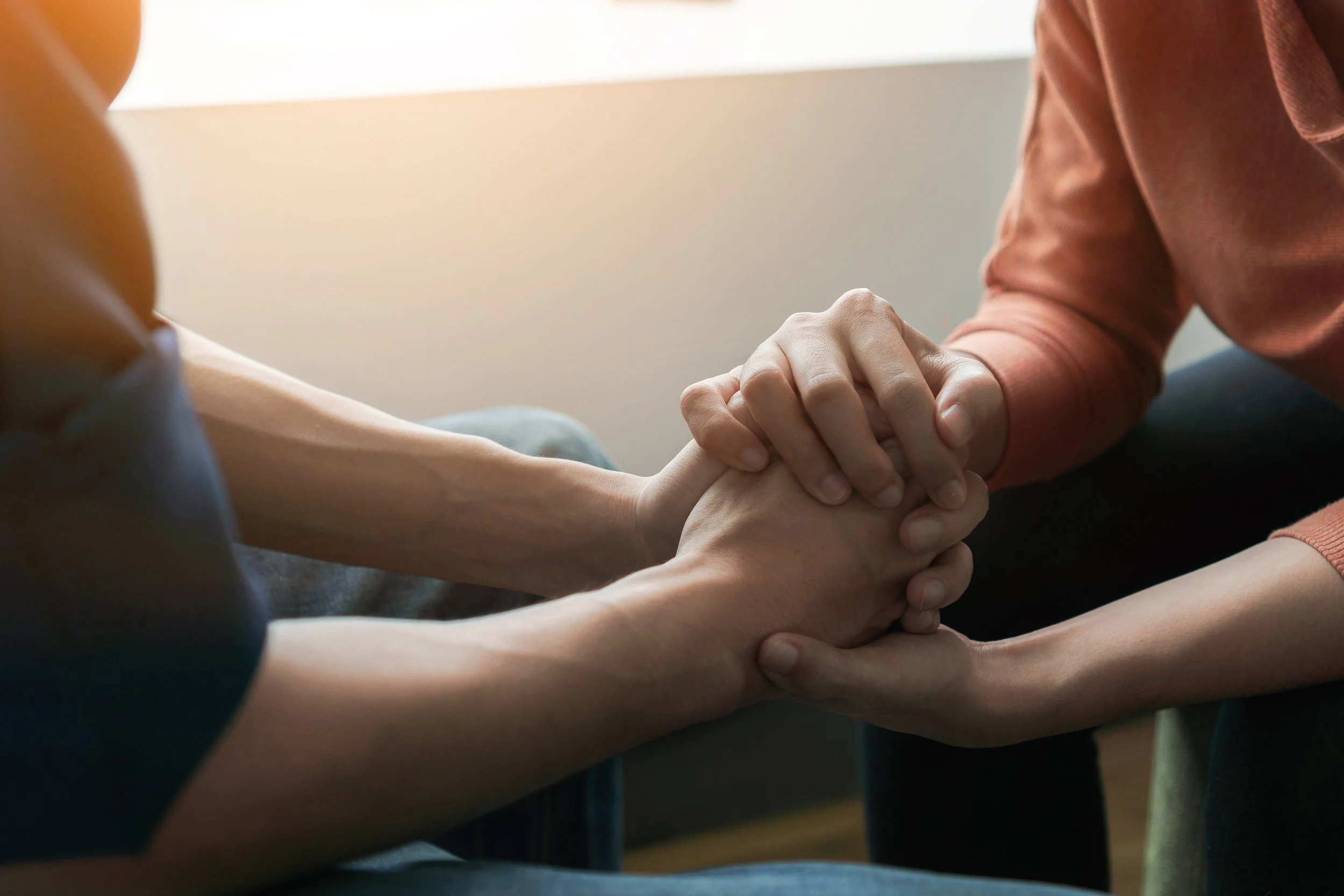 Two people holding hands in an emotional, supportive gesture indoors with natural light.