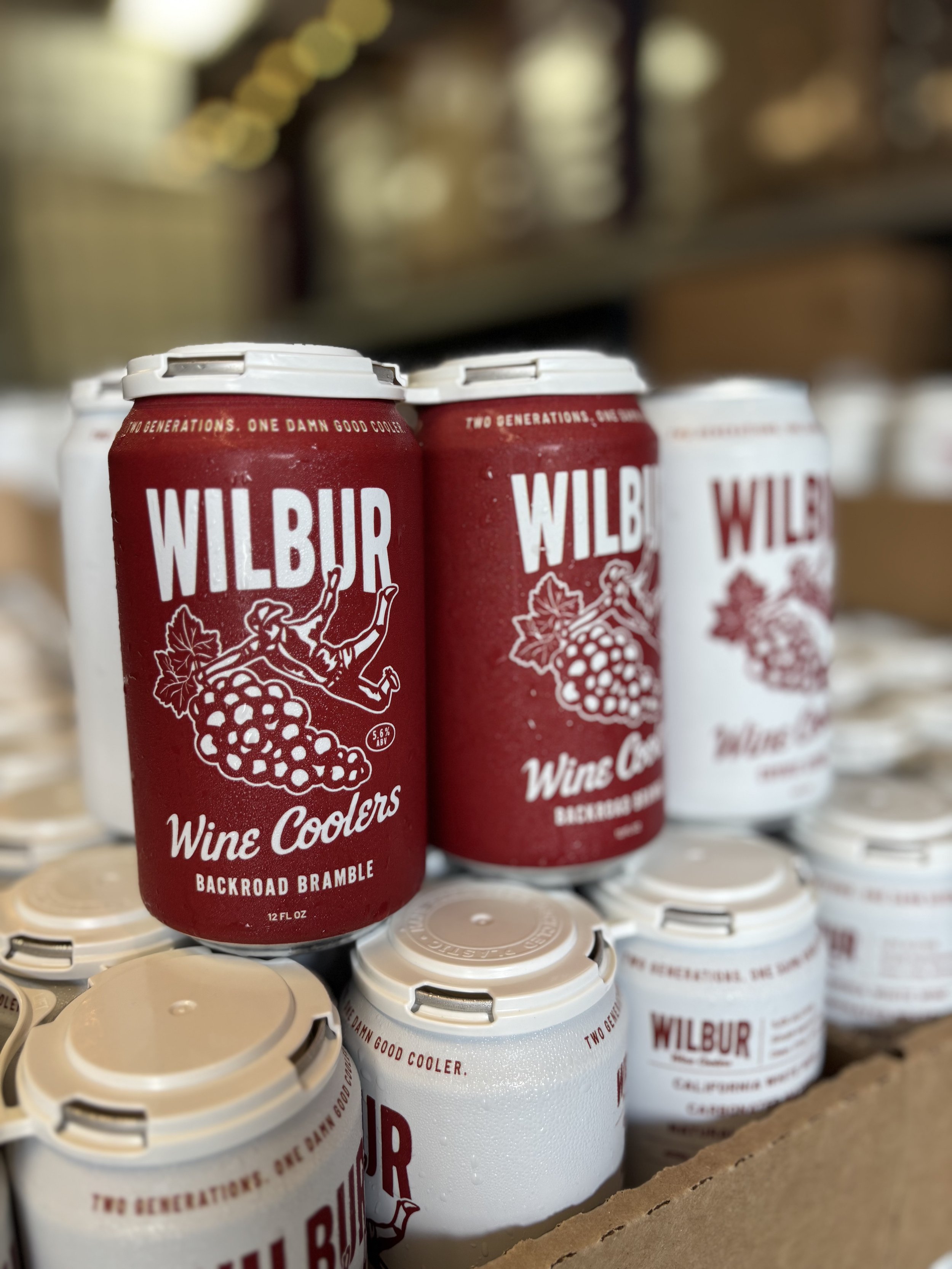 Cans of Wilbur wine coolers, with some cans in red and white packaging placed together on a surface.