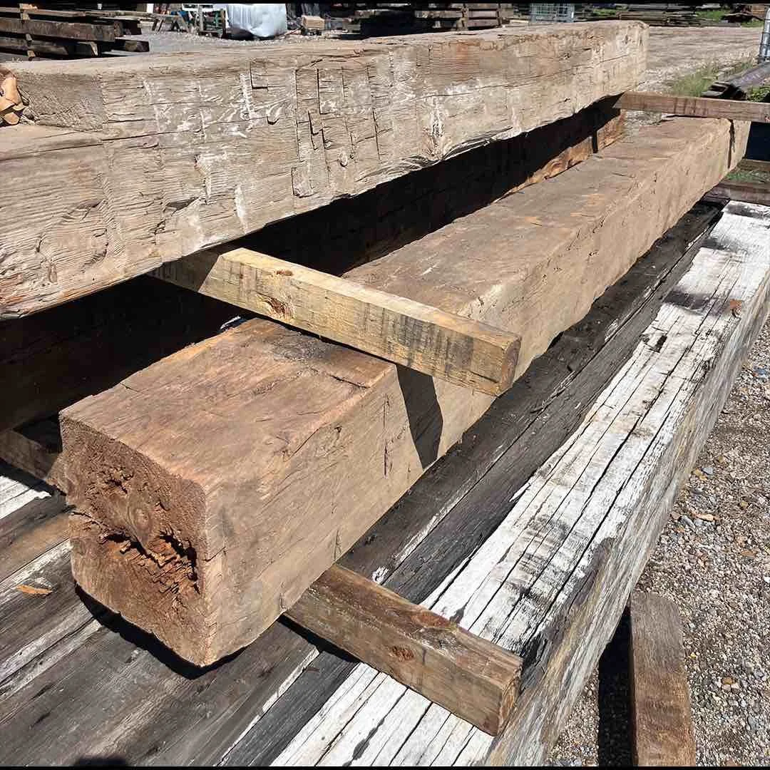 Thumbnail of antique reclaimed hand-hewn timbers stacked outdoors, with visible tool marks, adze cuts, and natural patina.
