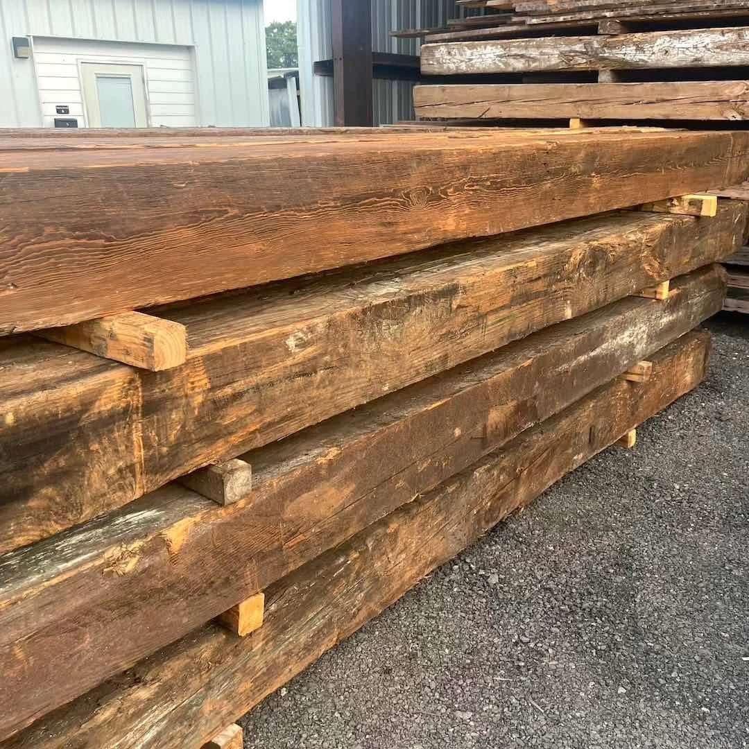 Stacked inventory of antique reclaimed industrial timbers with visible growth rings, aged texture, and natural patina.