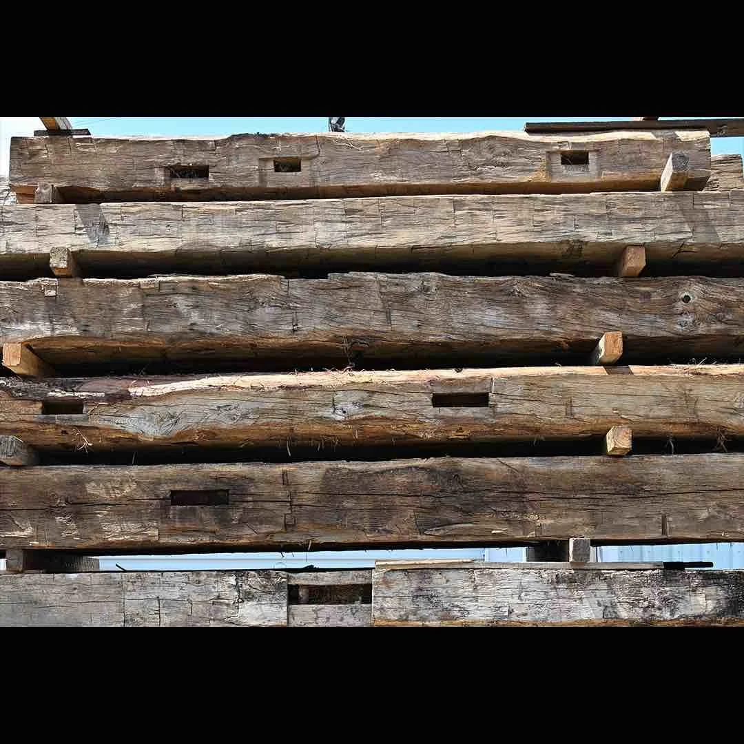 Thumbnail of stacked antique reclaimed hand-hewn timbers with visible tool marks, mortise pockets, and aged weathered surfaces.