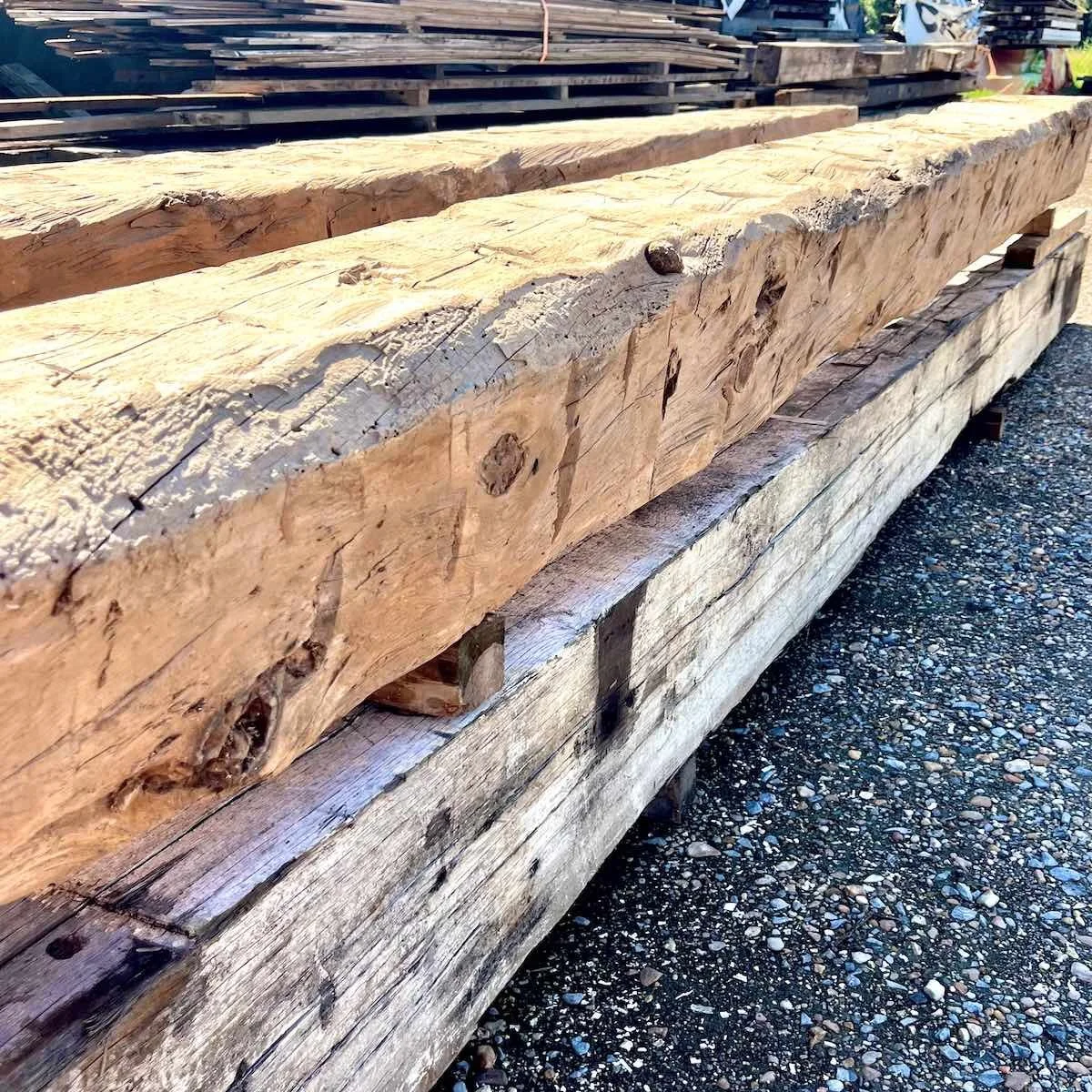 Antique reclaimed hand-hewn timbers with visible tool marks and aged patina stacked outdoors.