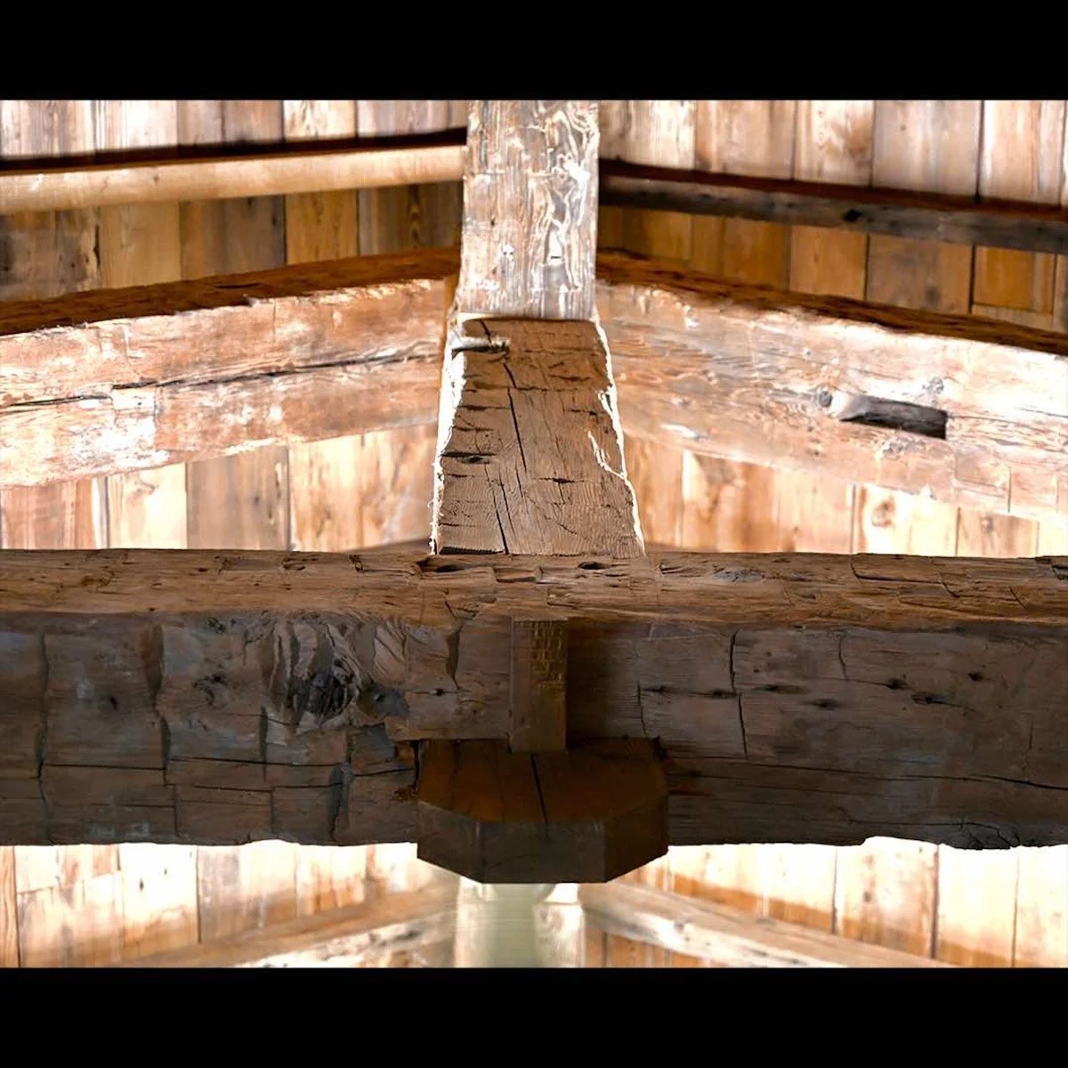 Exposed antique reclaimed hand-hewn timber truss with mortise and tenon joinery in a rustic wood ceiling.