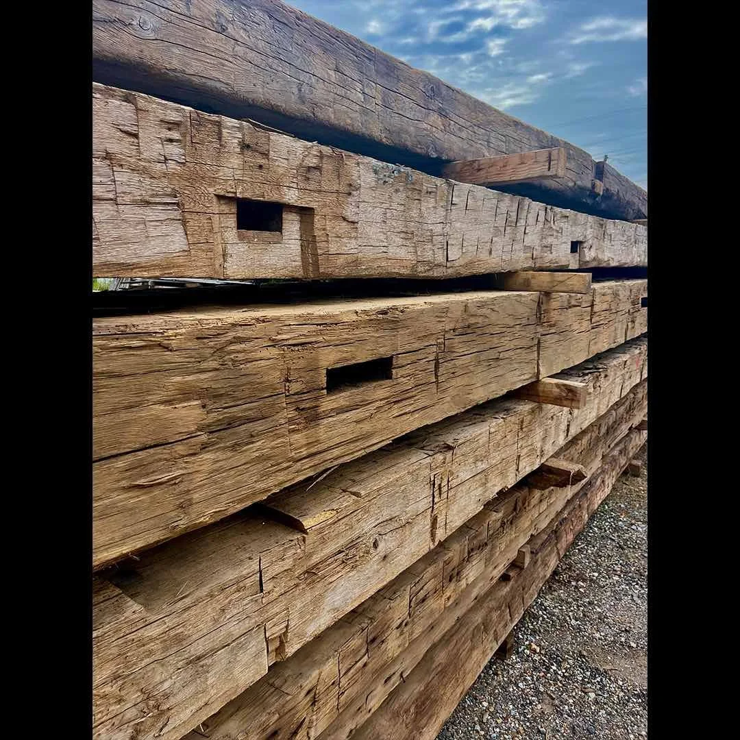 Thumbnail of antique reclaimed hand-hewn timbers with visible mortise pockets, stacked outdoors with aged patina.