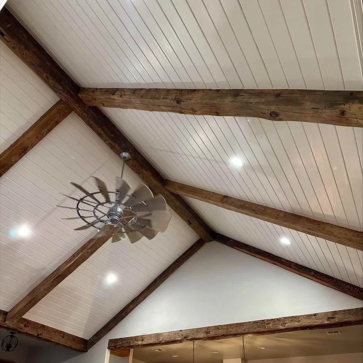Client home with exposed antique reclaimed hand-hewn timber ceiling beams, white panels, and farmhouse-style ceiling fan.