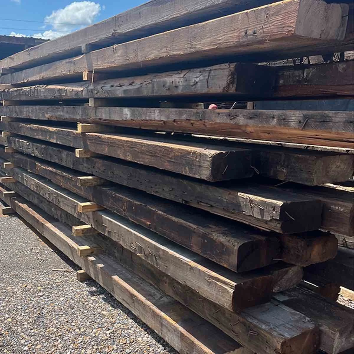Antique reclaimed industrial timbers stacked in rows with dark aged patina, weathered surfaces, and authentic old-growth character.