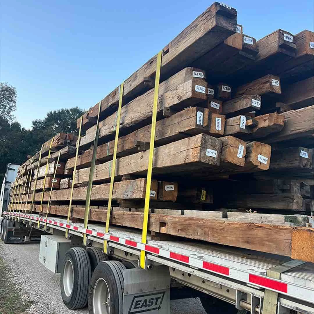 Thumbnail of antique reclaimed hand-hewn timbers loaded and strapped on a flatbed trailer for transport, showing timbers with dimension tags.