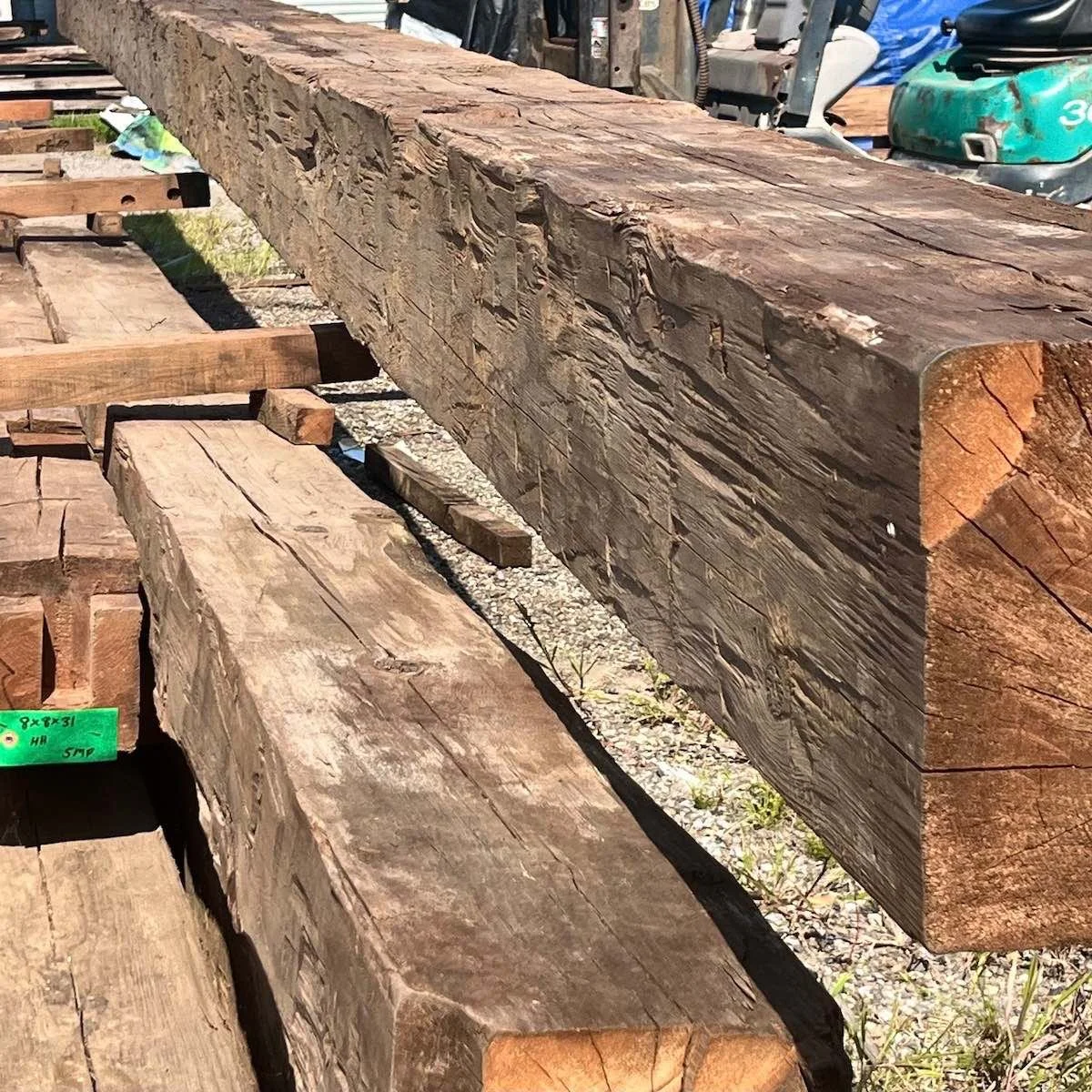 Antique reclaimed hand-hewn timber beams stacked outdoors, showing tool marks and weathered patina.