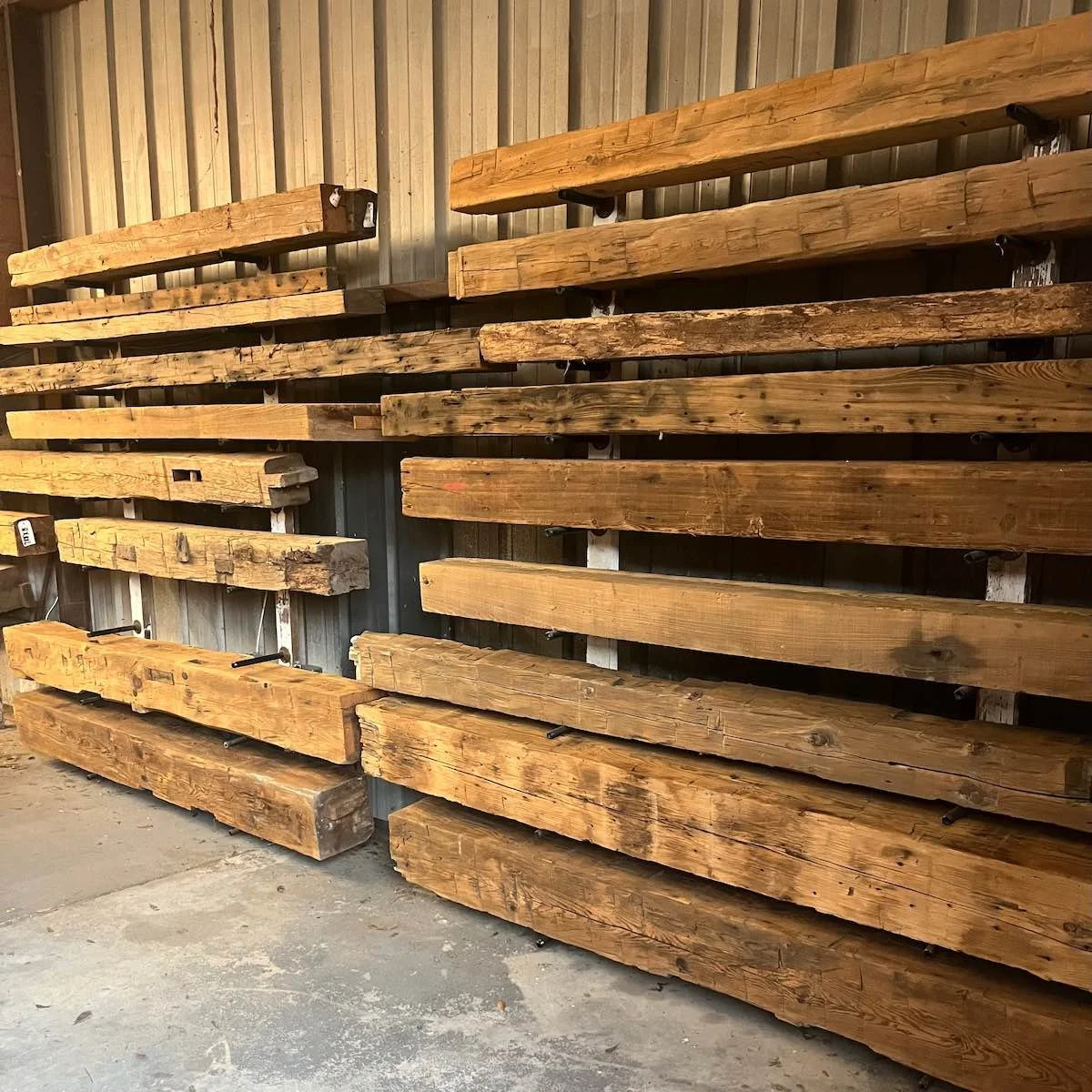 Antique reclaimed beam mantels, stacked on the wall, showcasing natural patina and weathered surface texture.
