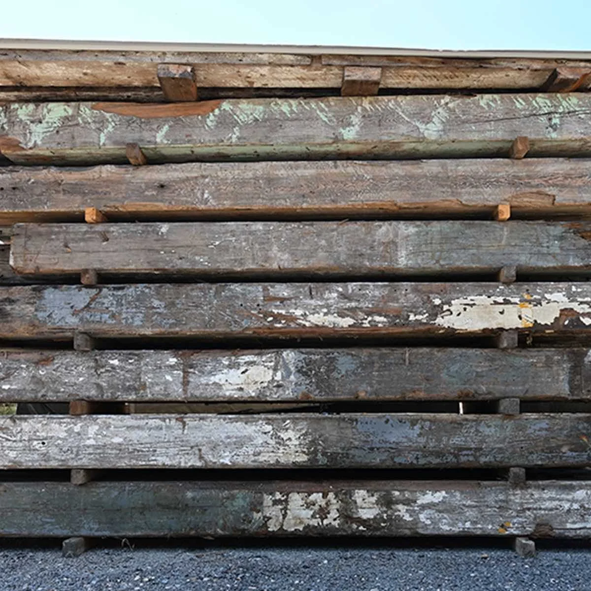 Stacked antique reclaimed industrial timbers with aged paint, weathered patina, and rustic texture.