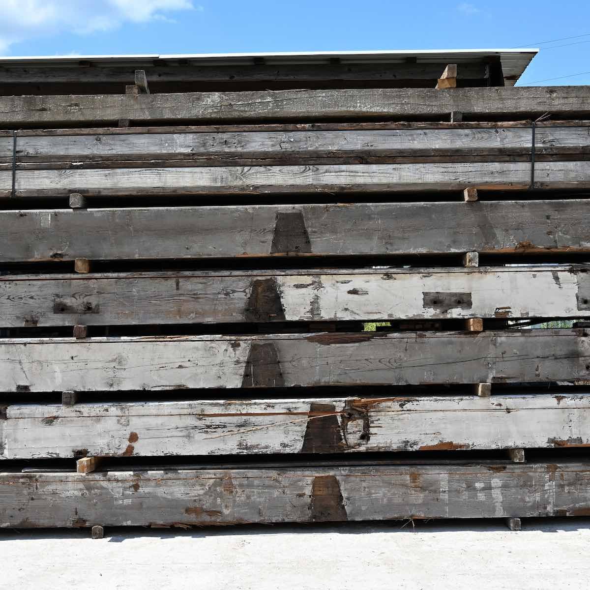 Weathered antique reclaimed industrial timbers stacked for reuse, showing aged paint and historic character.