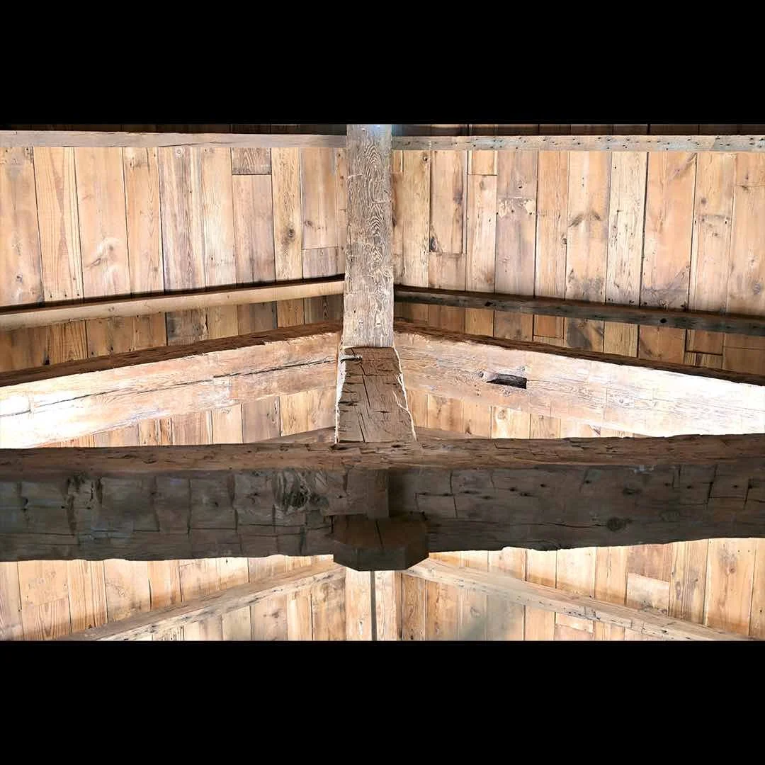 Exposed antique reclaimed hand-hewn timber truss system with visible mortise and tenon joint on a rustic wood ceiling.