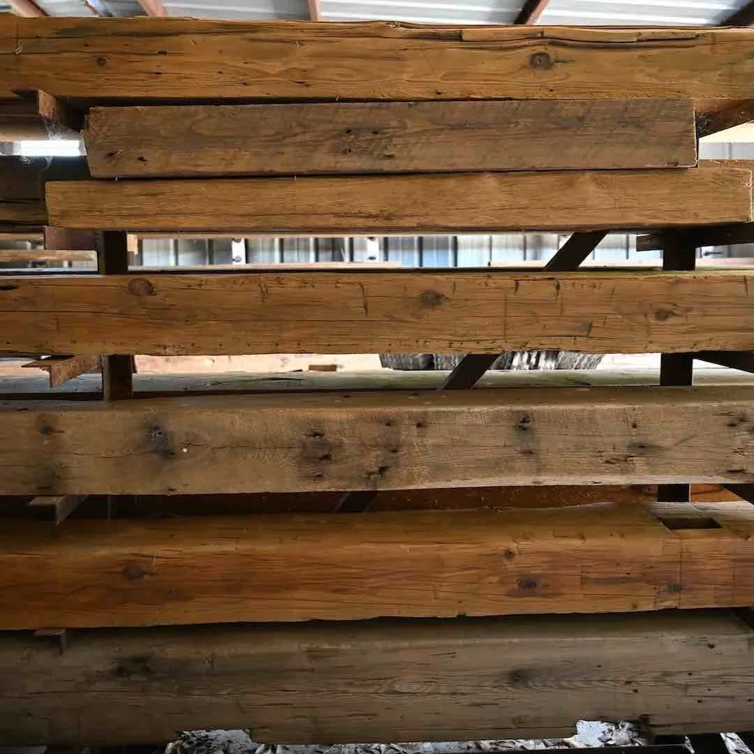 Stacked short timbers of varying dimension showing natural patina, nail holes, tool marks, and aged texture.