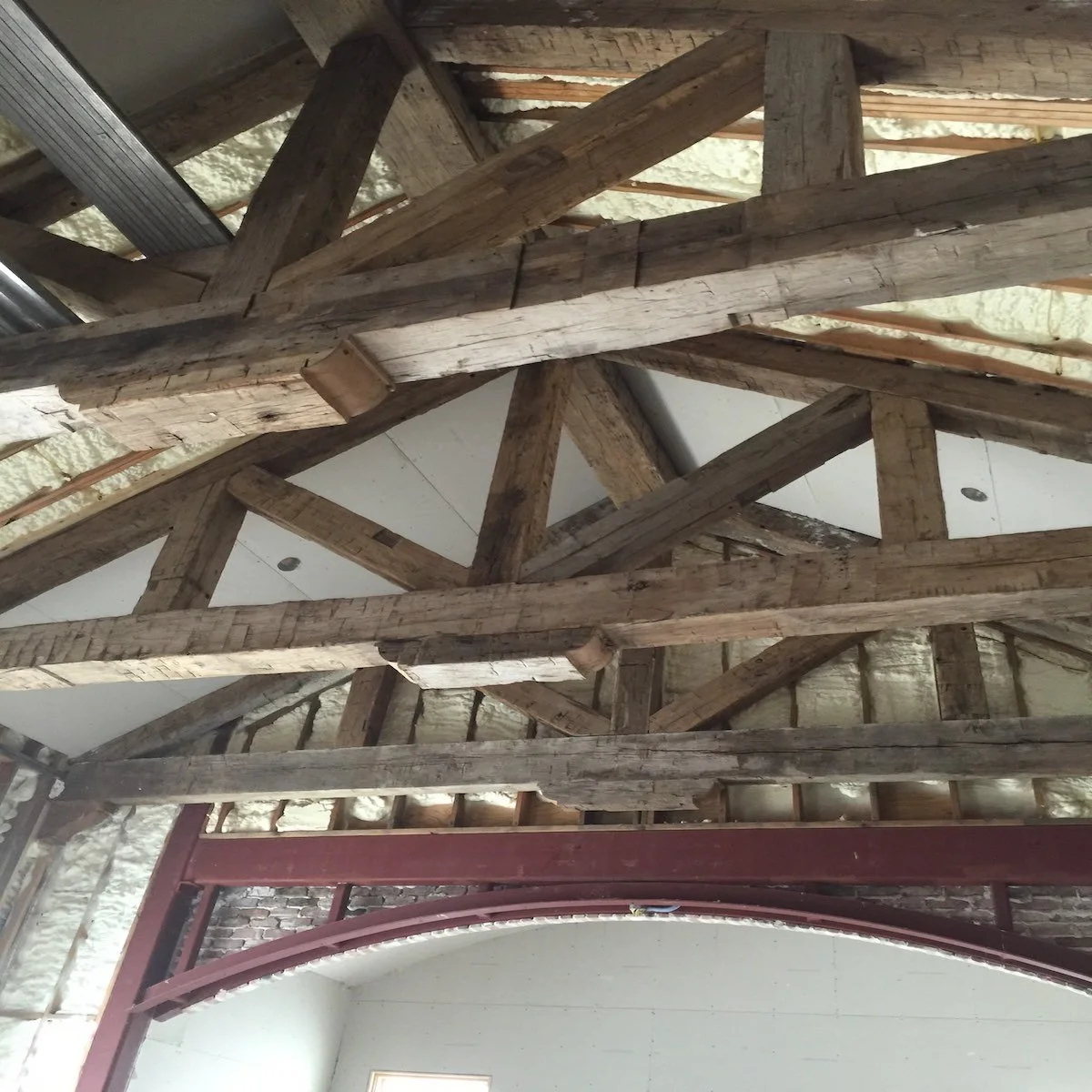 Client installation with antique reclaimed hand-hewn timber frame trusses, showing exposed tool marks and rustic character in vaulted ceiling construction.