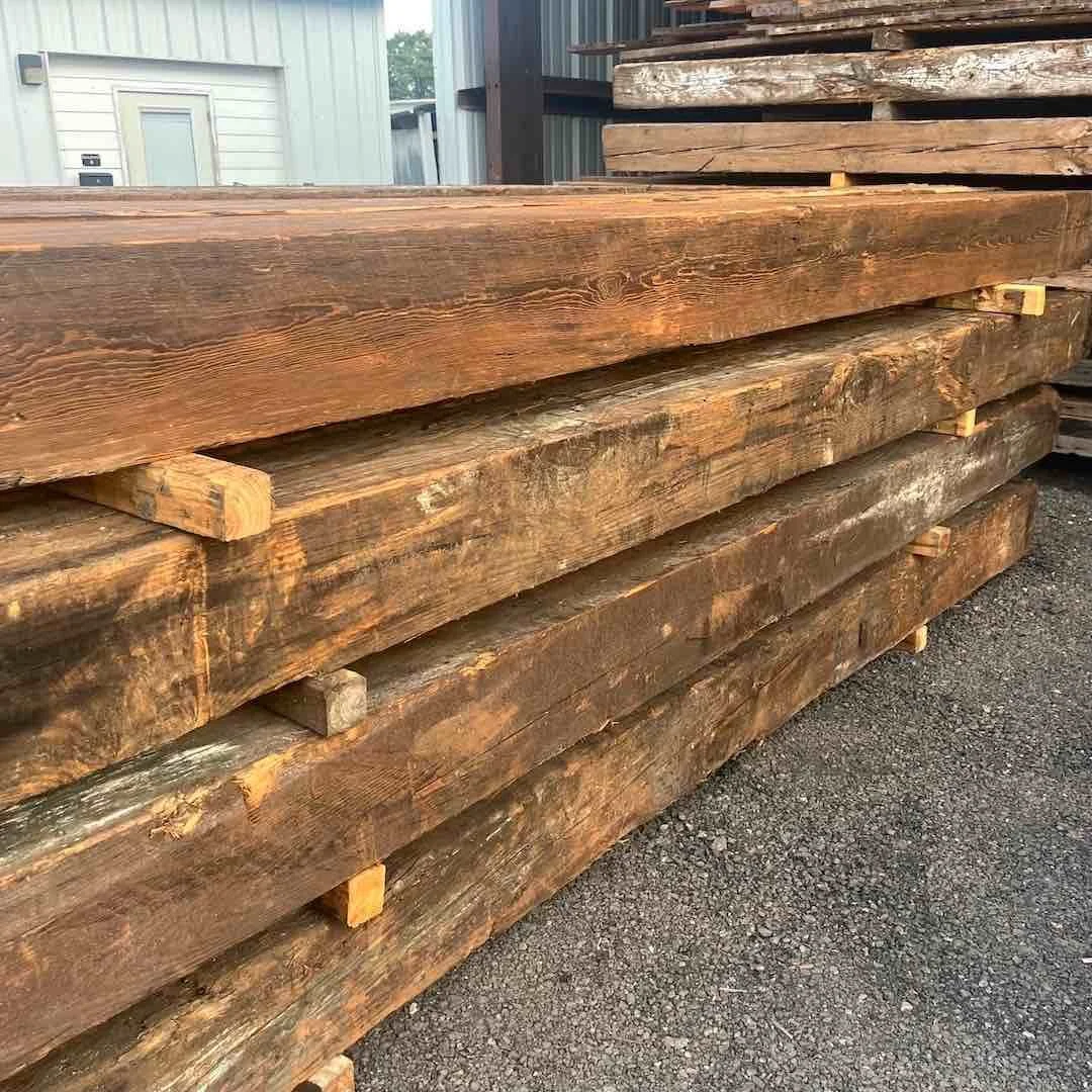 Stacked antique reclaimed industrial timbers, primarily longleaf pine, showing aged patina and rough sawn texture.